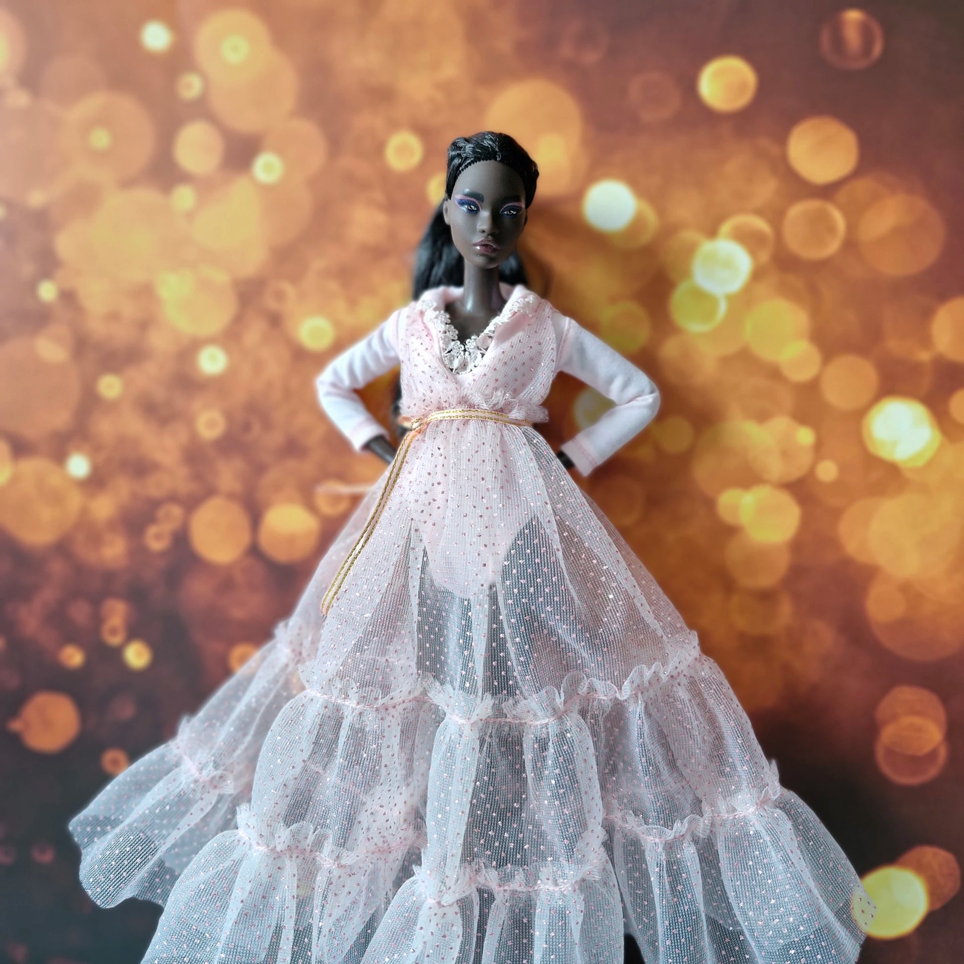 Front view of dark-skinned Barbie doll in elegant pink tiered tulle gown with gold belt accent.