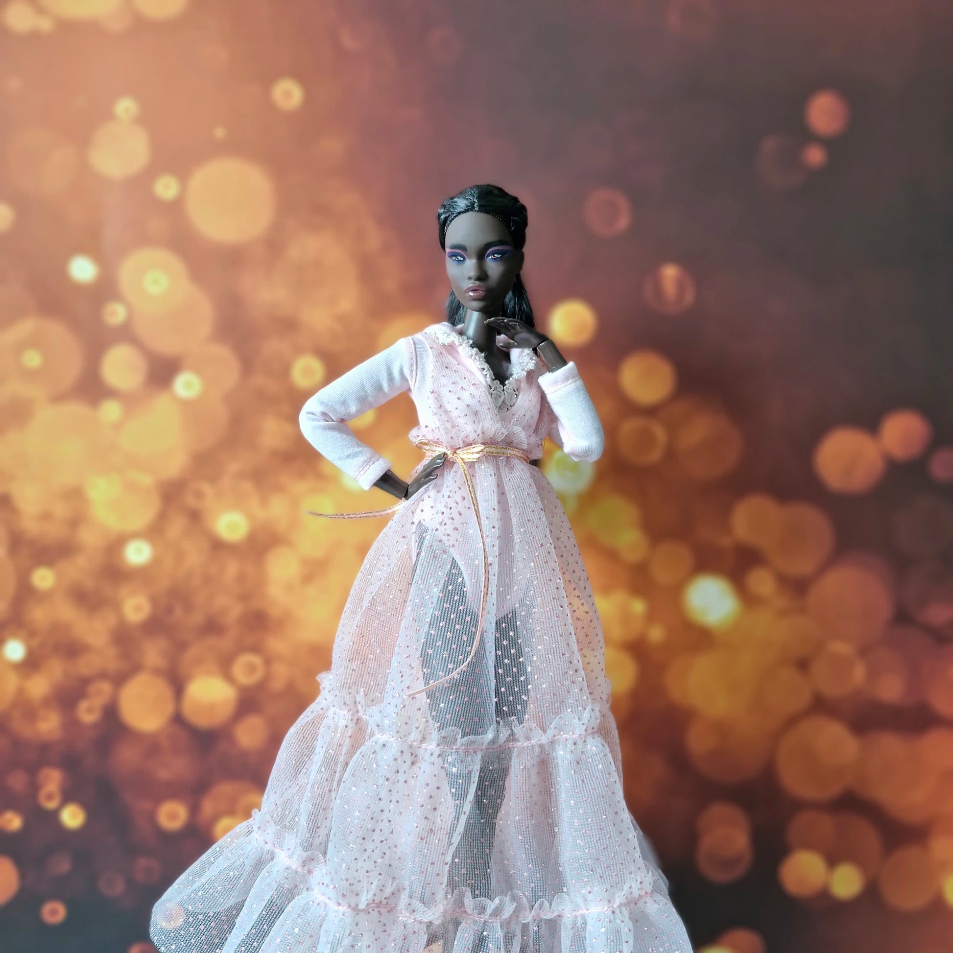 Dark-skinned Barbie doll posing in sophisticated pink tiered sparkle tulle gown with gold ribbon belt.