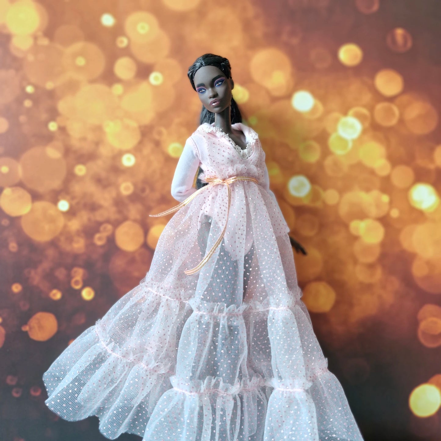 Dark-skinned Barbie doll looking elegant in pink sparkly tiered tulle gown with long sleeves and gold belt.