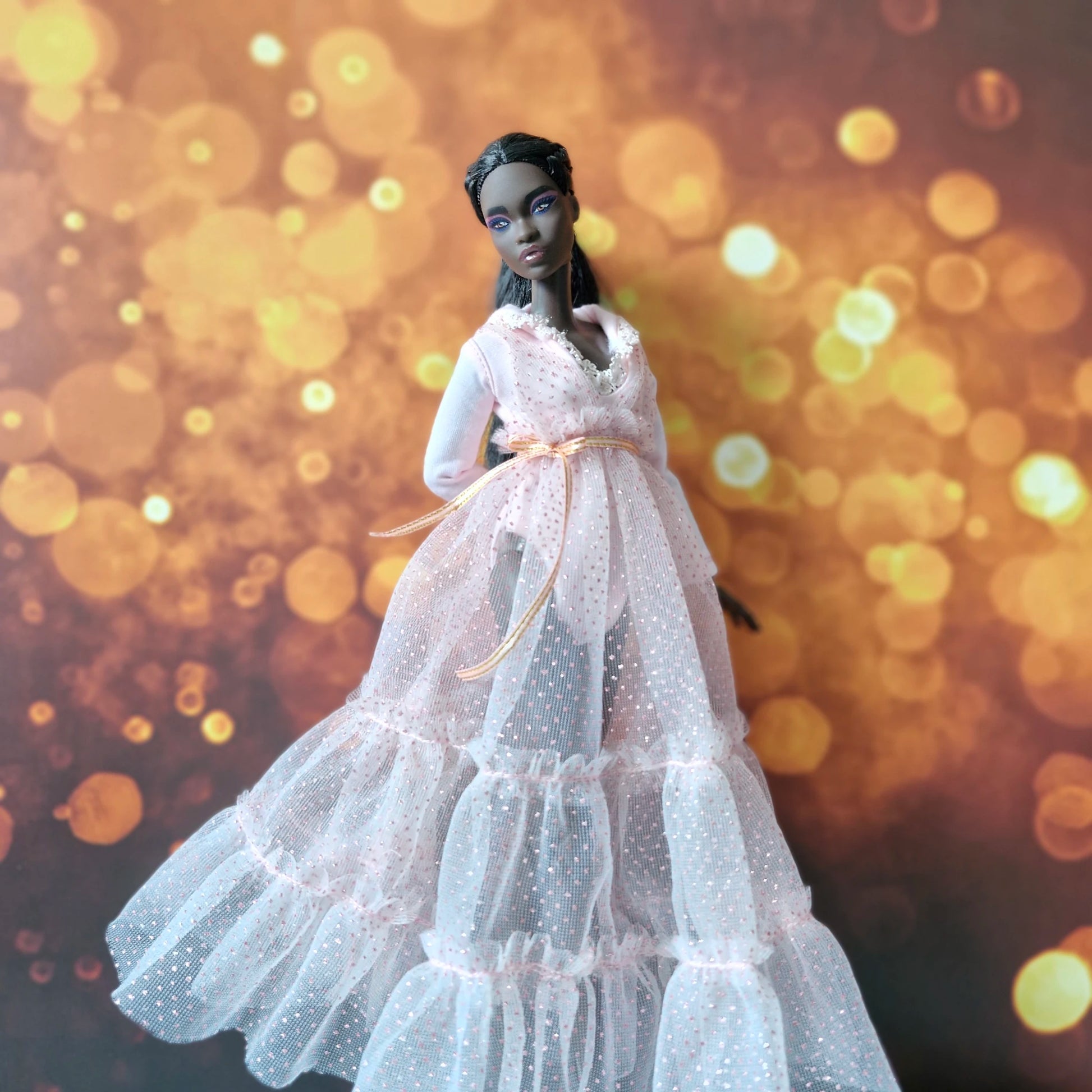 Dark-skinned Barbie doll looking elegant in pink sparkly tiered tulle gown with long sleeves and gold belt.