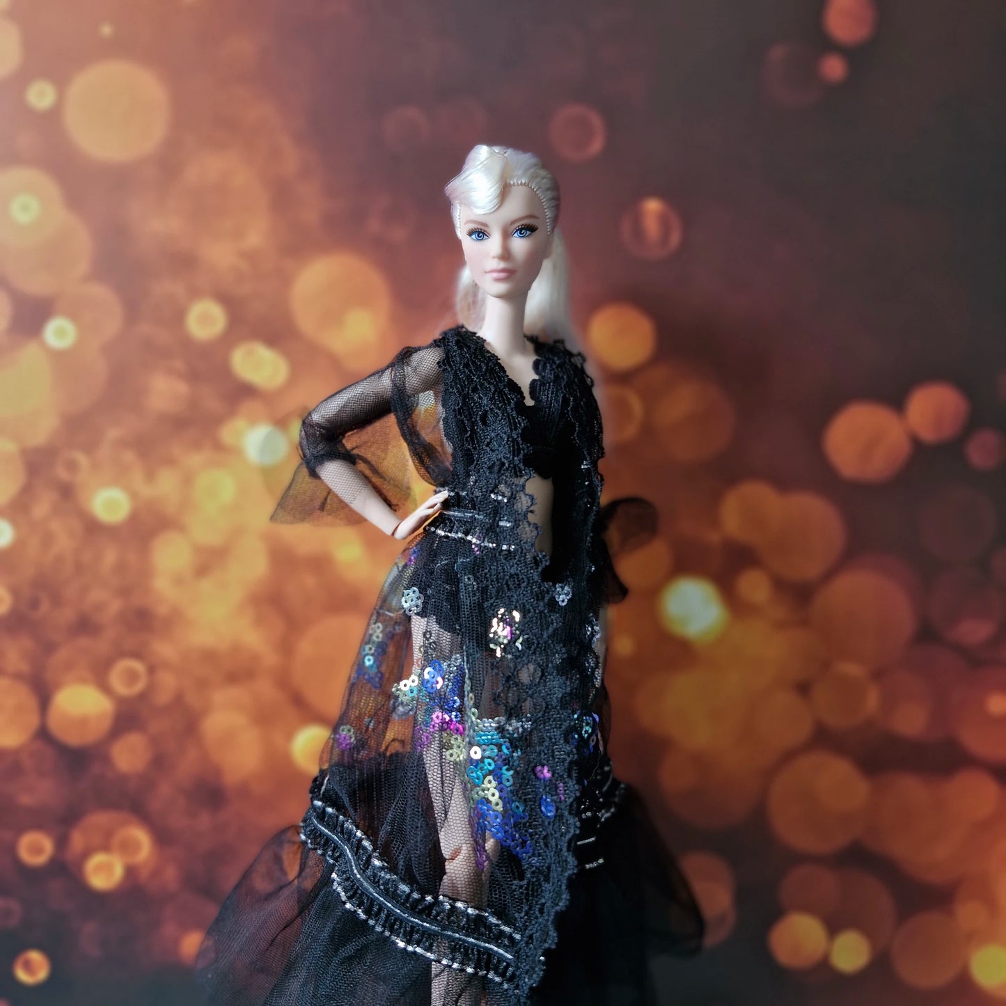 Side profile of blonde Barbie doll in glamorous black sheer lace and sequin overlay gown.