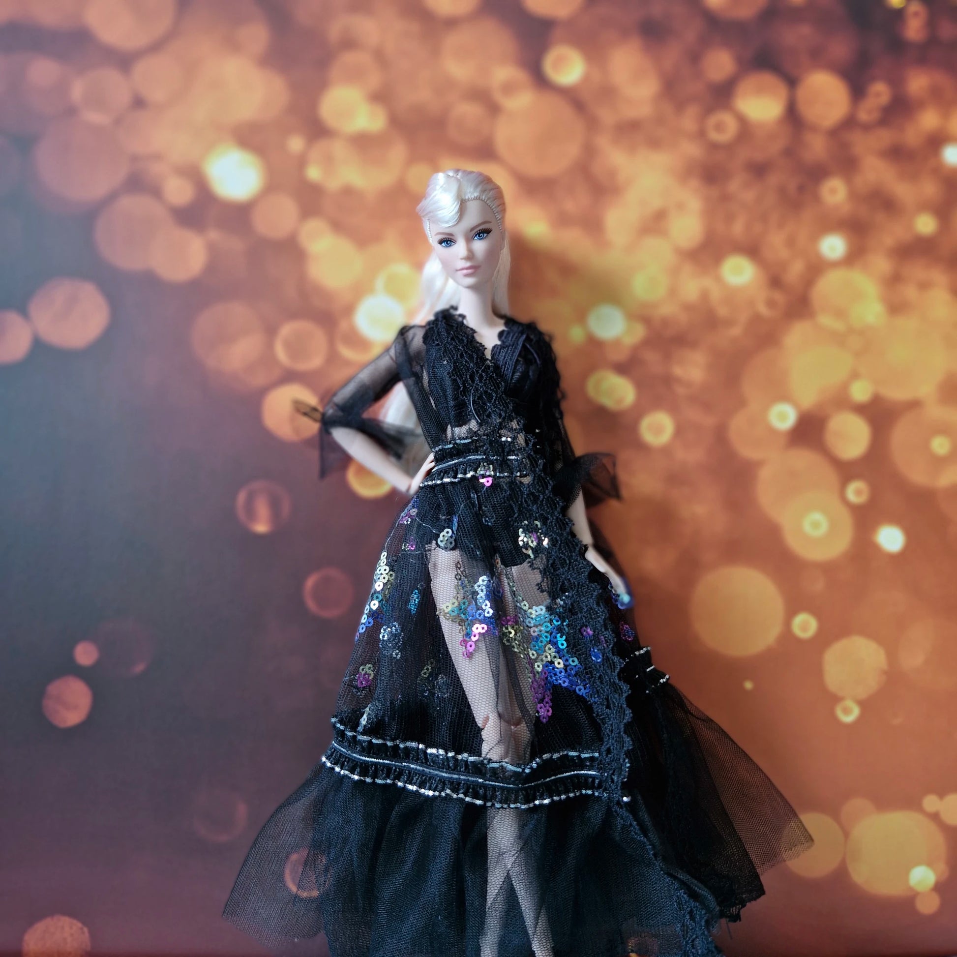 Blonde Barbie doll wearing sophisticated black sheer gown with sequin details and lace trim.