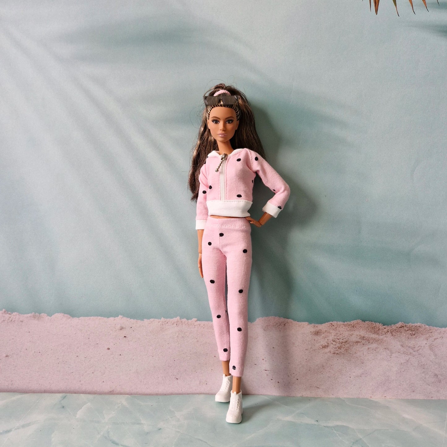 Barbie doll wearing pink polka dot tracksuit and white sneakers, beach background.