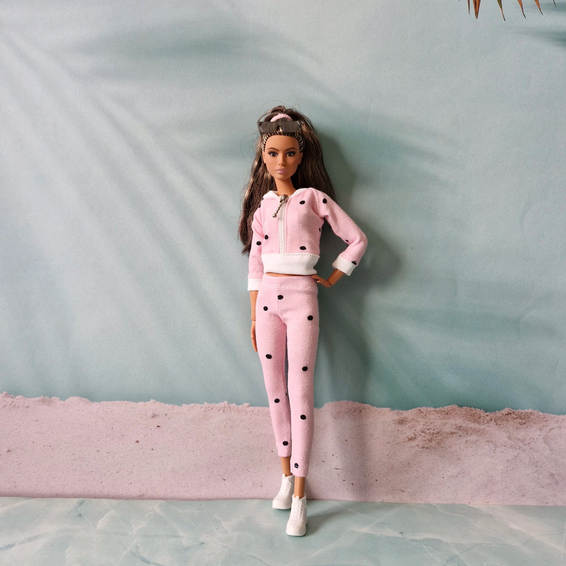 Barbie doll wearing pink polka dot tracksuit and white sneakers, beach background.
