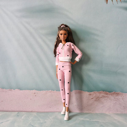Barbie doll wearing pink polka dot tracksuit and white sneakers, beach background.