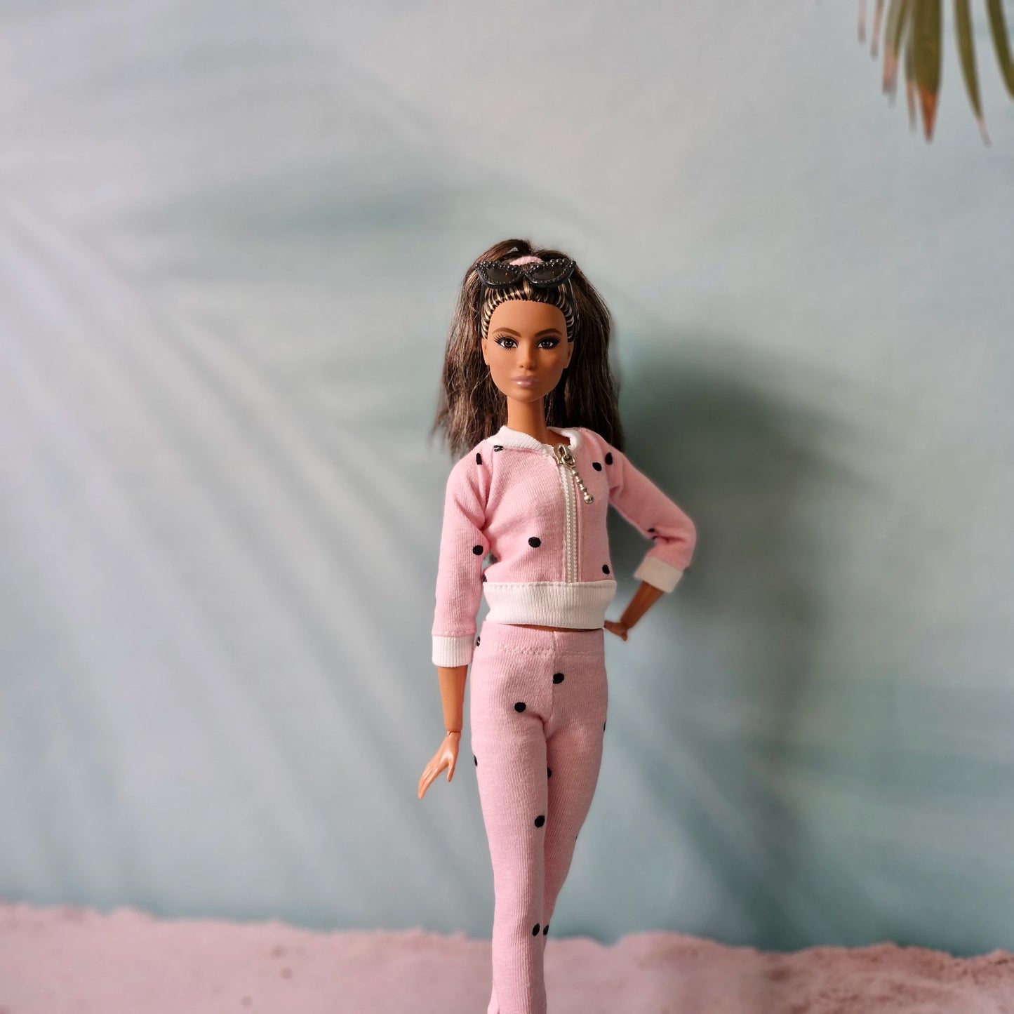 Close-up of Barbie doll in pink polka dot tracksuit with sunglasses headband, casual style.