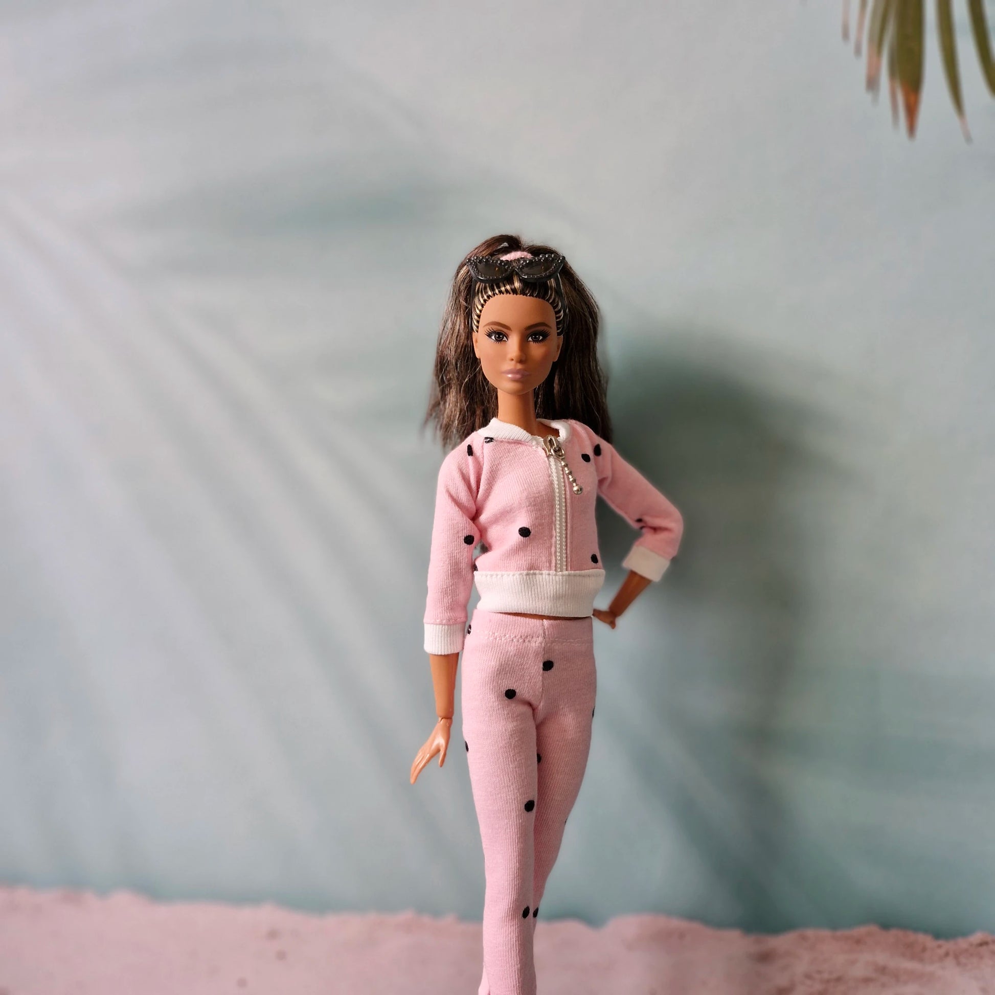 Close-up of Barbie doll in pink polka dot tracksuit with sunglasses headband, casual style.
