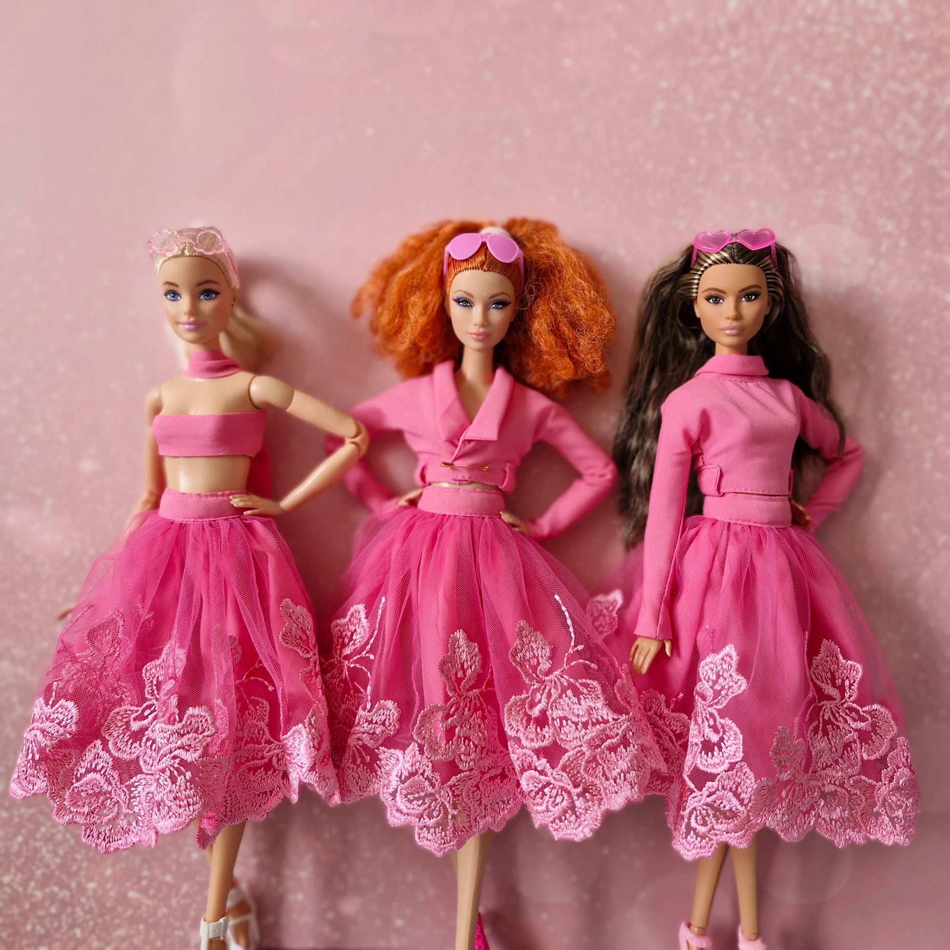 Three Barbie dolls (blonde, red-haired, brunette) modeling different pink outfit combinations.