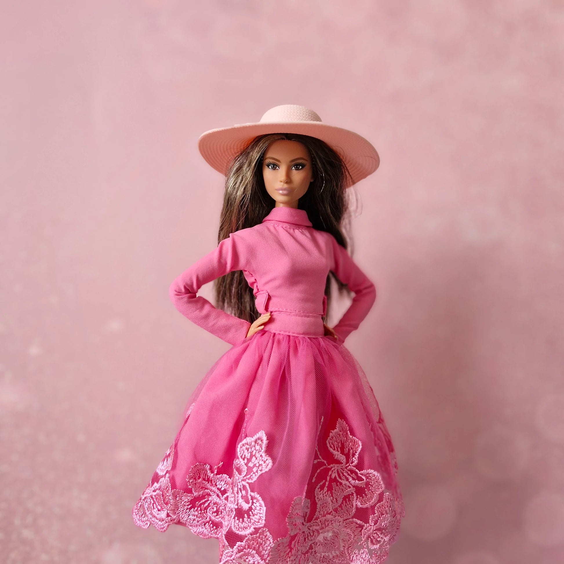 Brunette Barbie doll wearing pink mock neck top, lace tulle skirt, and pink sun hat.
