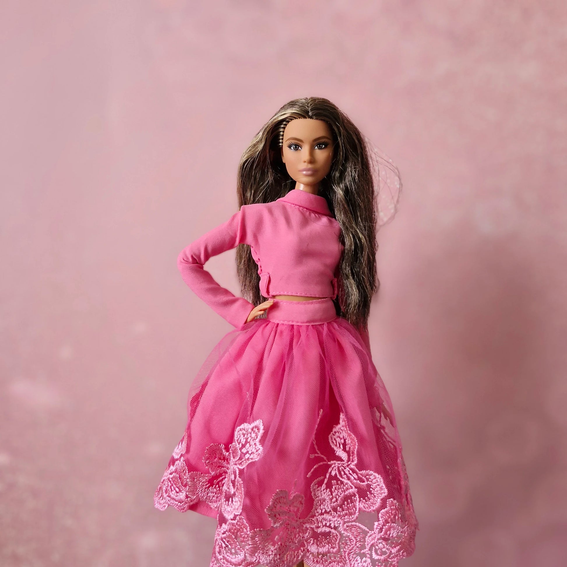 Brunette Barbie doll in pink mock neck top and pink lace tulle skirt, pink background.