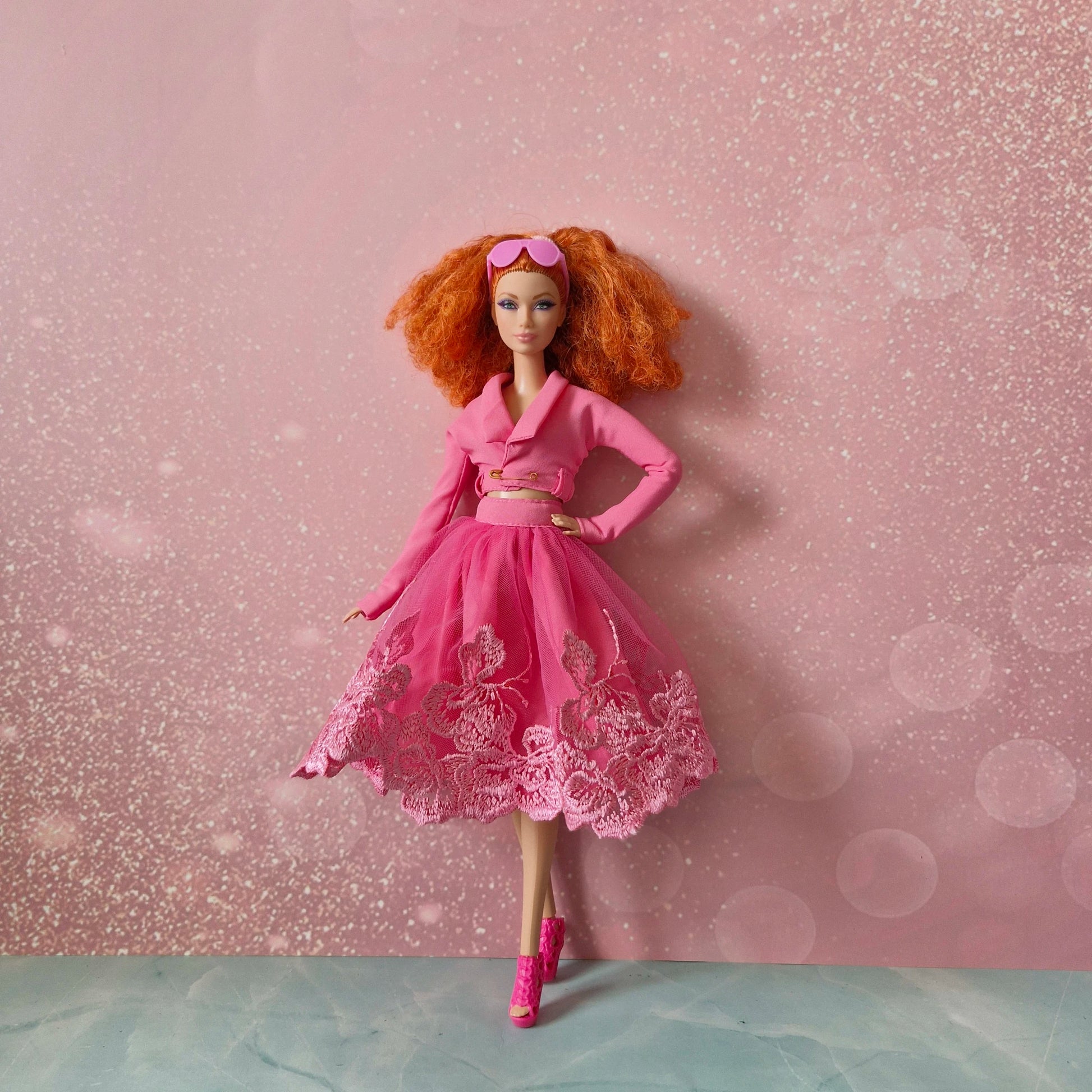 Red-haired Barbie doll in pink cropped jacket, lace tulle skirt, and pink heels.
