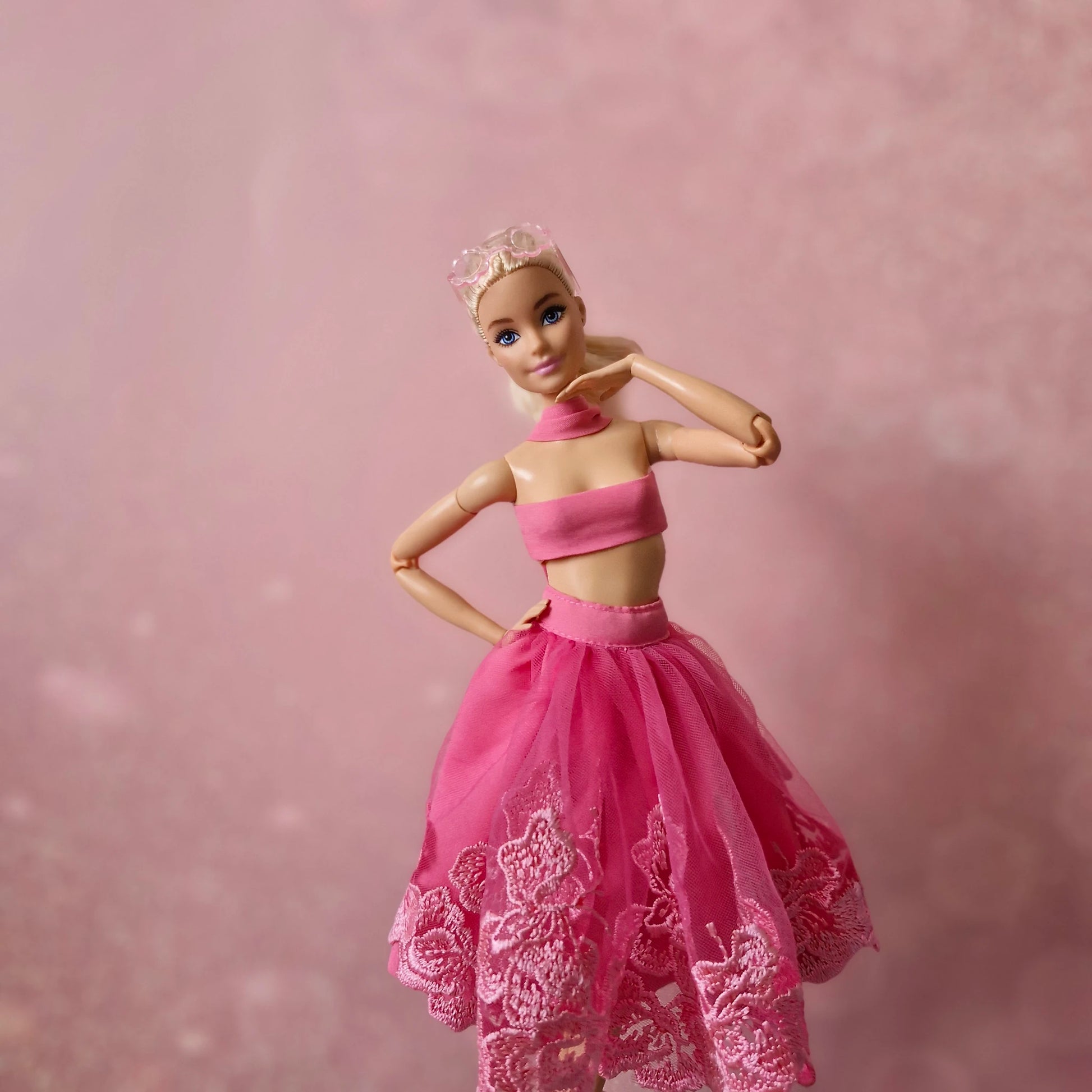 Blonde Barbie doll in pink bandeau top and pink lace tulle skirt, tiara, pink background.