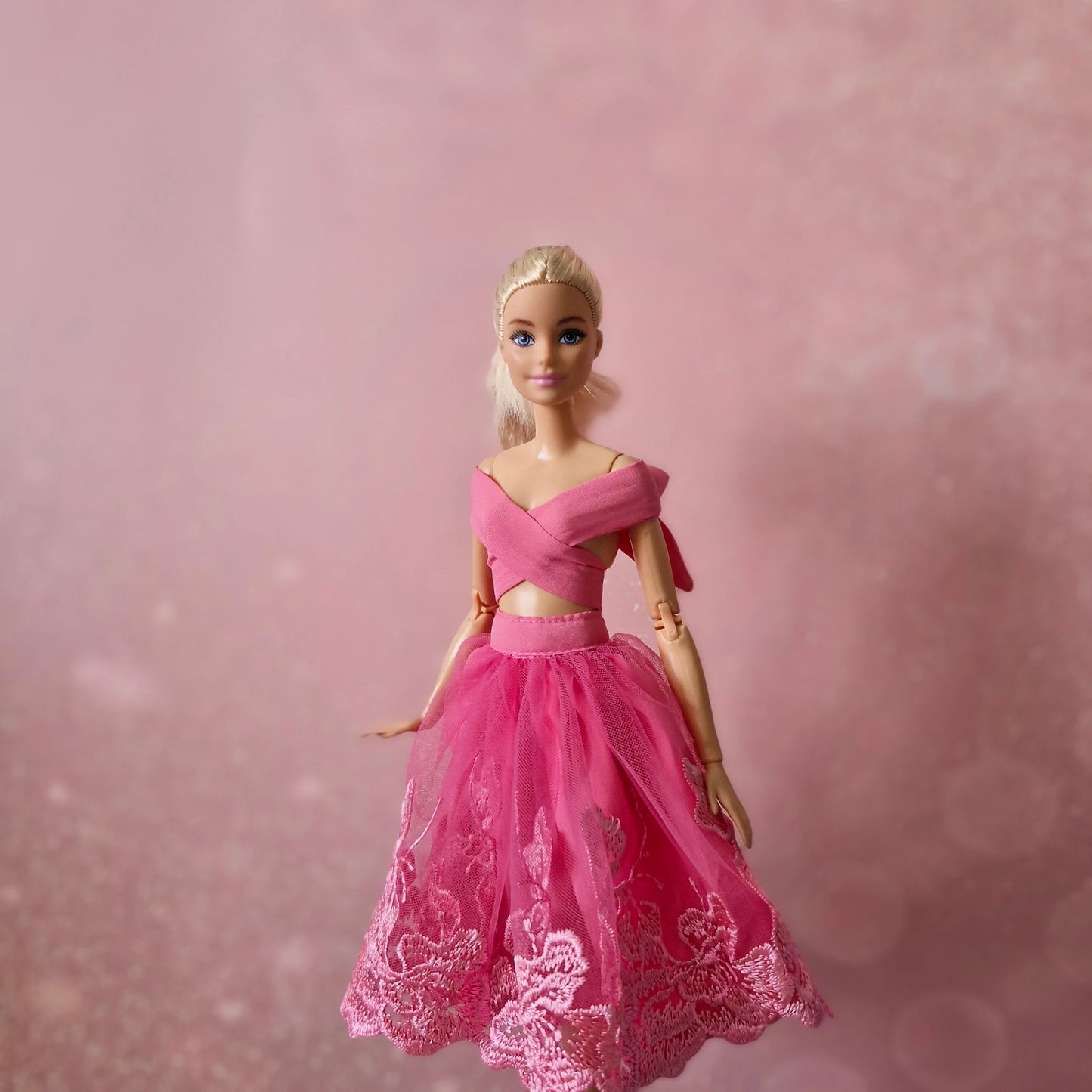 Blonde Barbie doll in pink criss-cross wrap top and pink lace tulle skirt, elegant pose.
