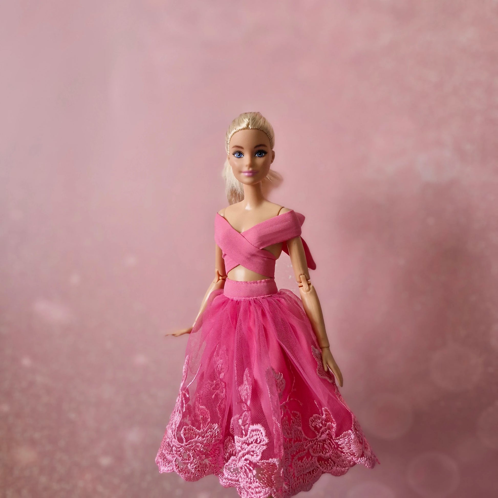 Blonde Barbie doll in pink criss-cross wrap top and pink lace tulle skirt, elegant pose.