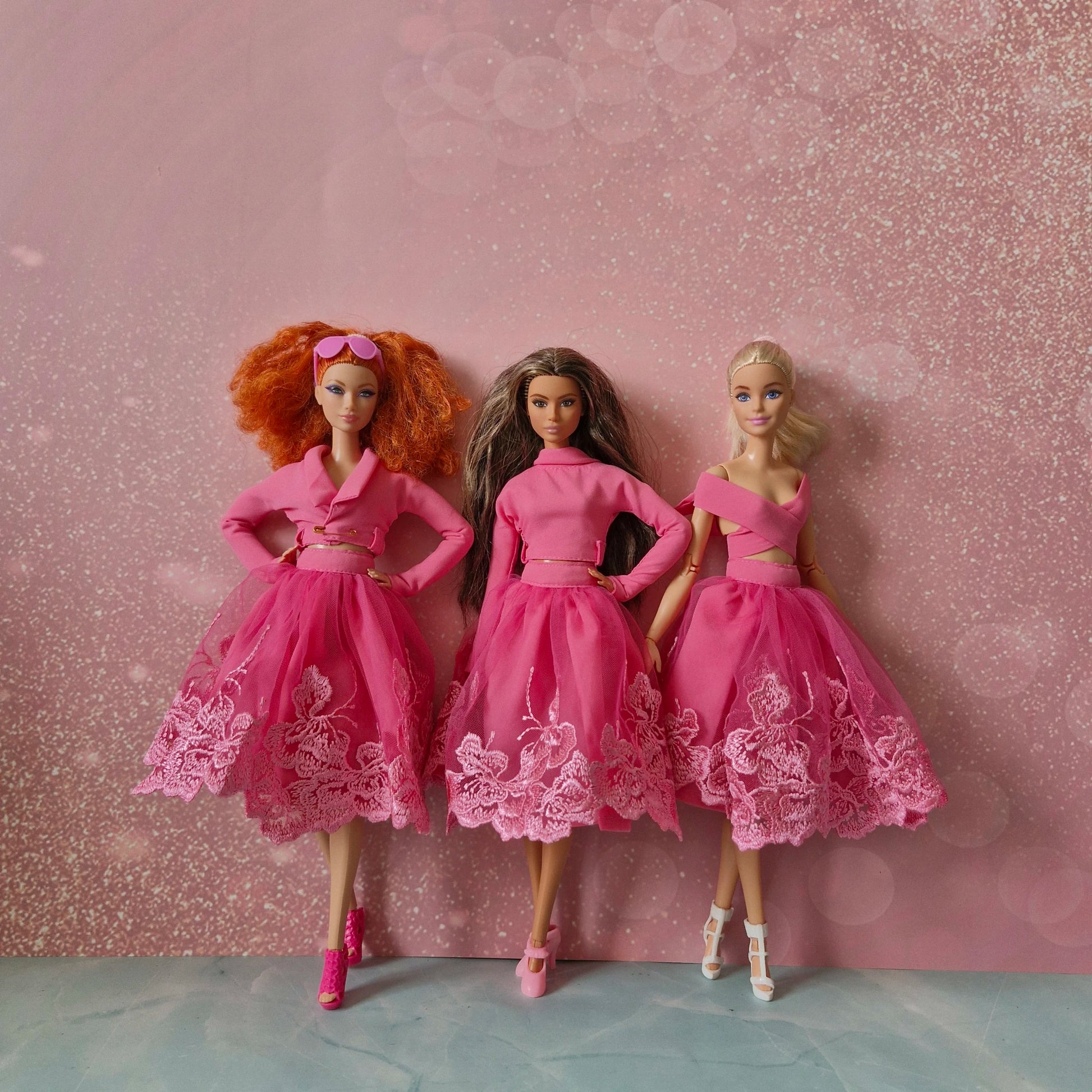 Three Barbie dolls (red-haired, brunette, blonde) in various pink lace skirt outfit styles.