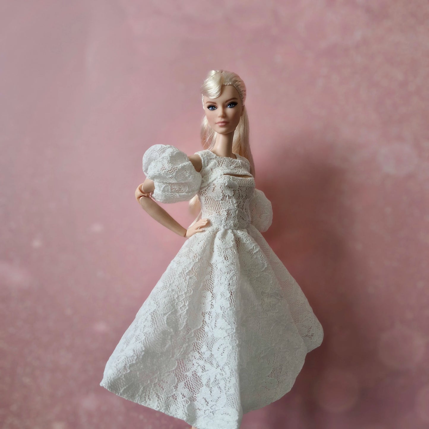 Blonde Barbie wearing white lace puff sleeve dress against a soft pink background.