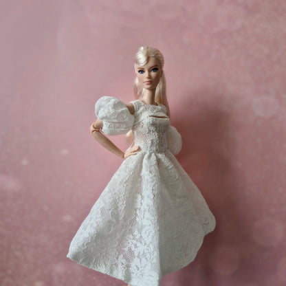 Blonde Barbie wearing white lace puff sleeve dress against a soft pink background.