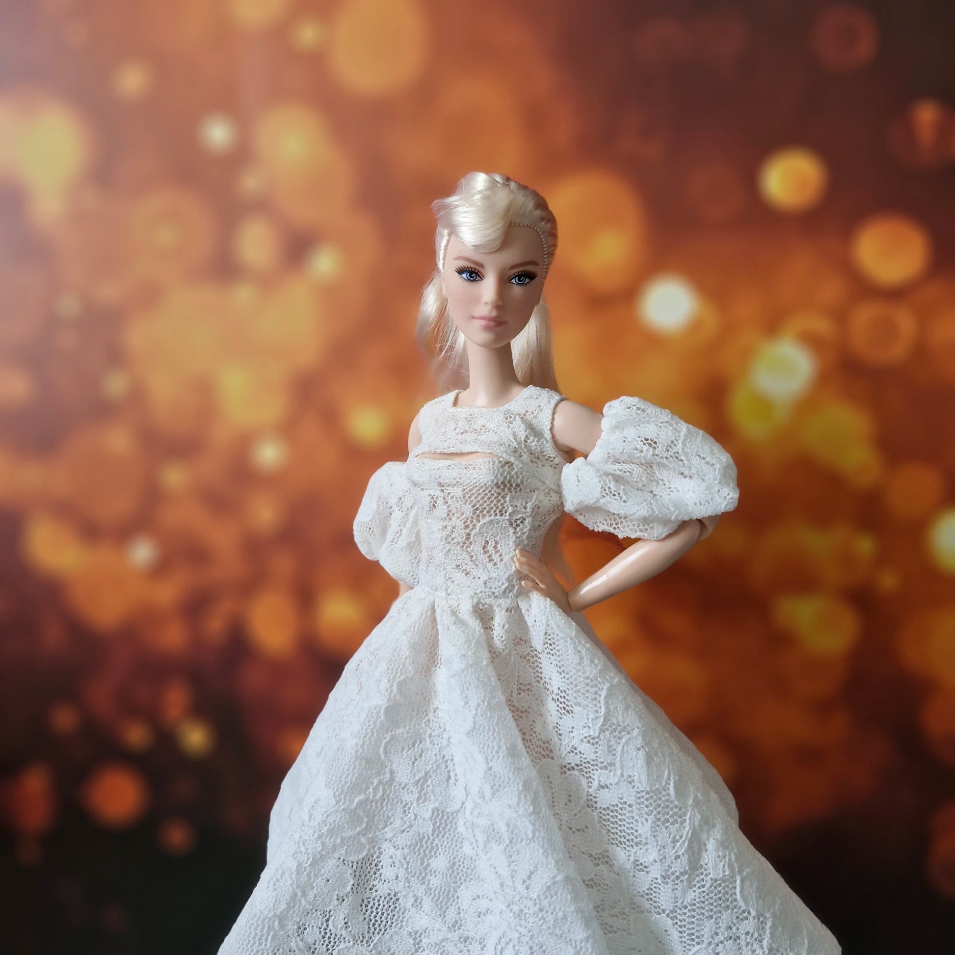 Blonde Barbie doll models elegant white lace dress with puff sleeves, bokeh background.
