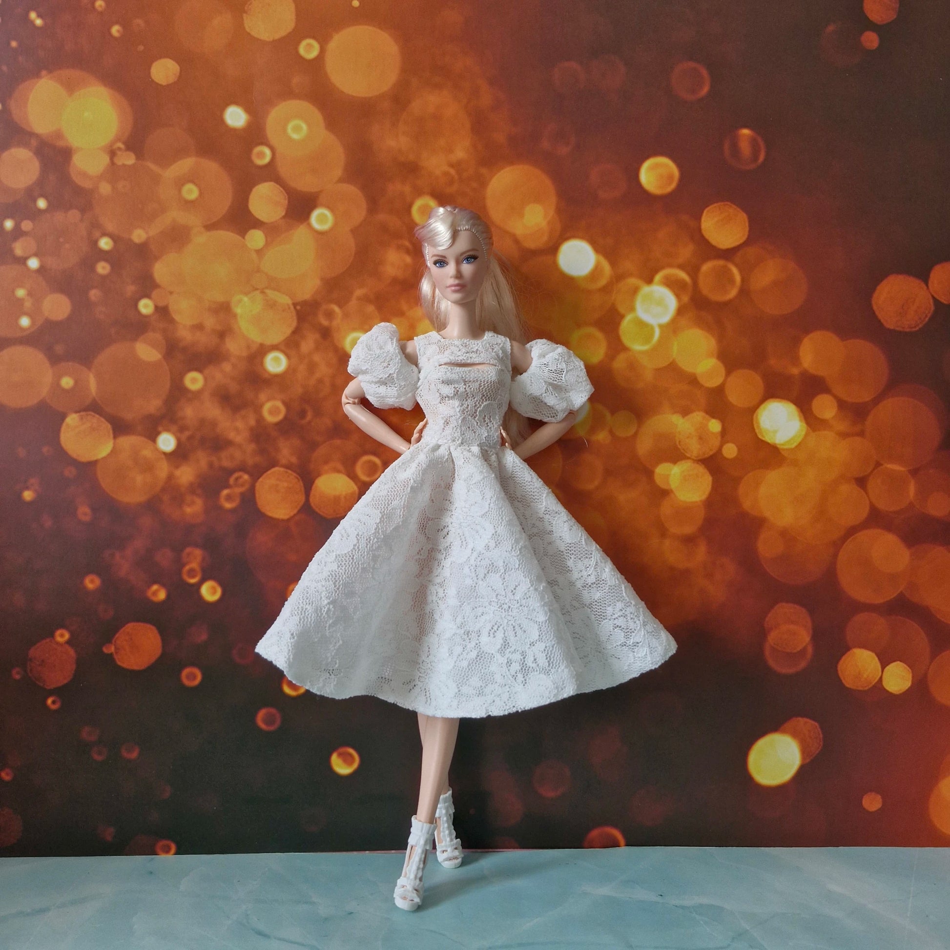 Full view of blonde Barbie doll in white lace dress with puff sleeves and white heels.
