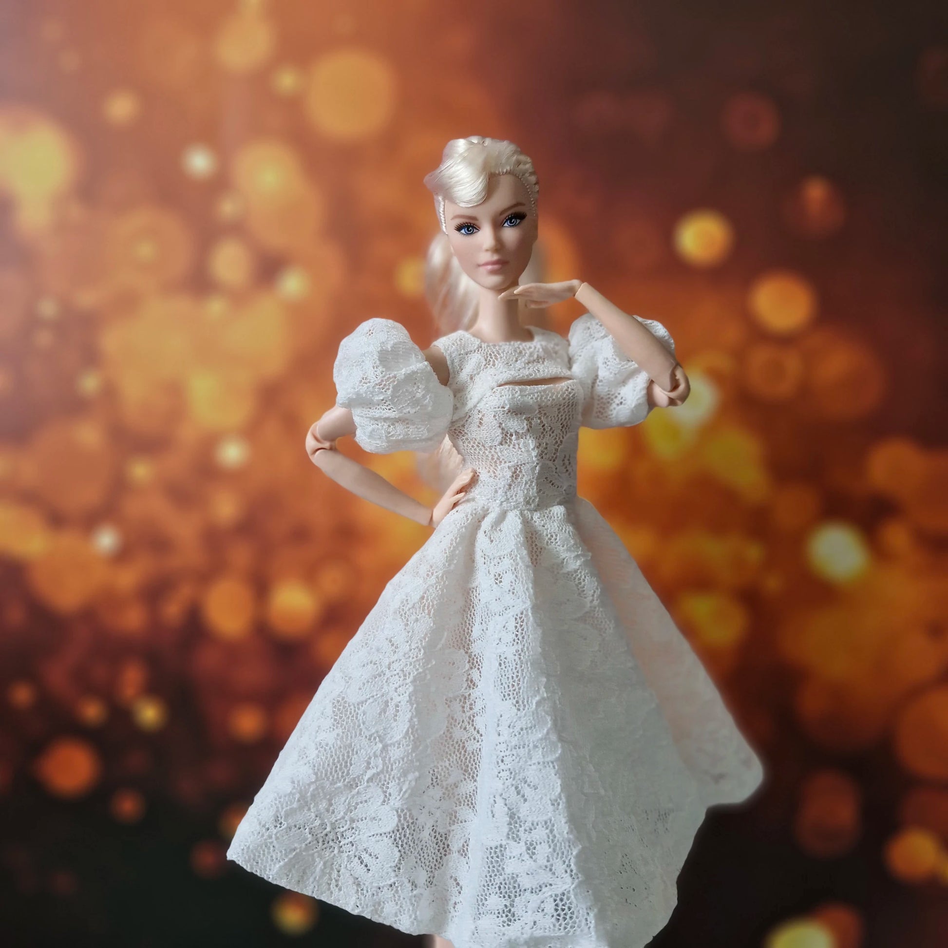 Blonde Barbie posing gracefully in white lace dress with puff sleeves, hand to face.