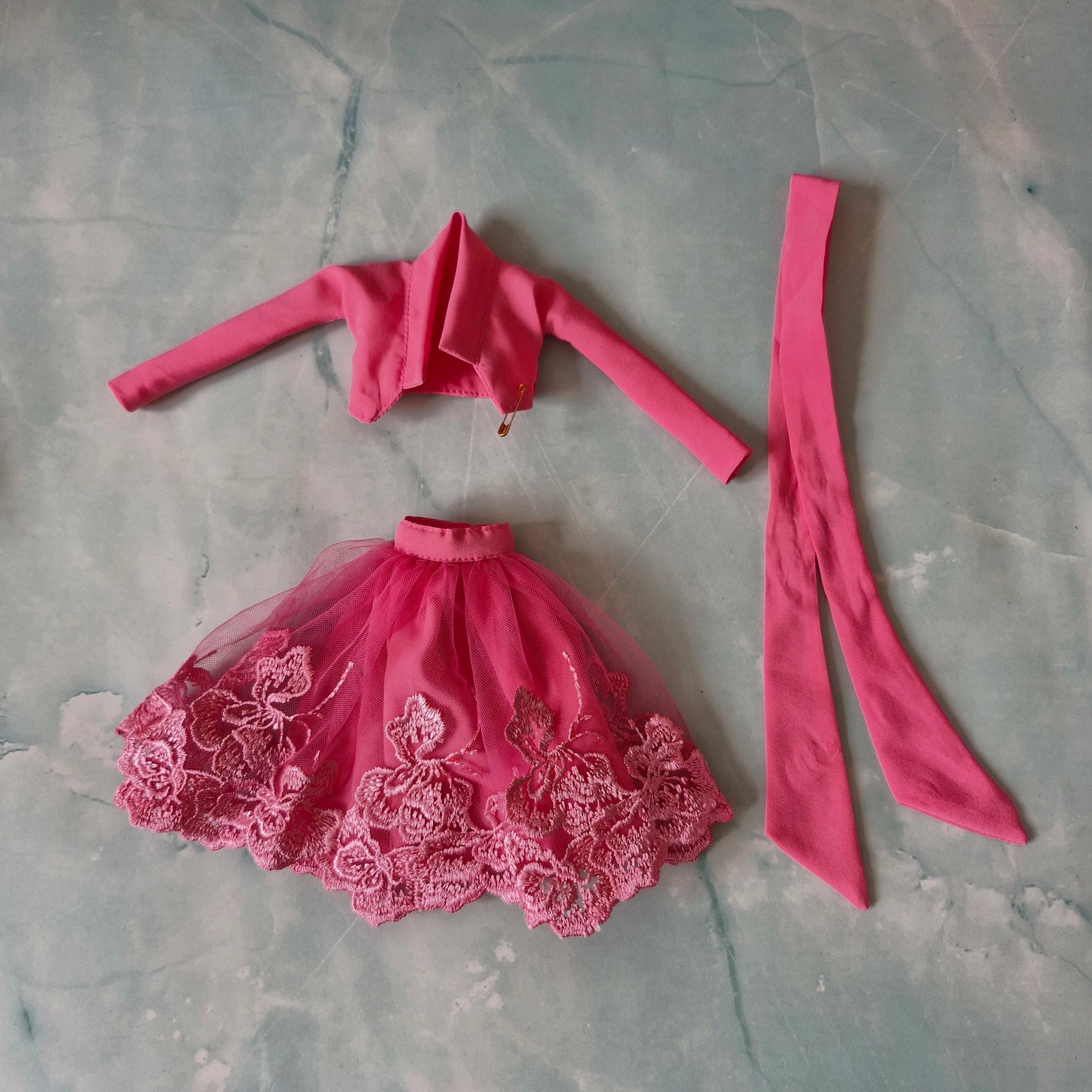 Flat lay of Barbie pink lace tulle skirt, pink cropped jacket, and pink fabric strip top.