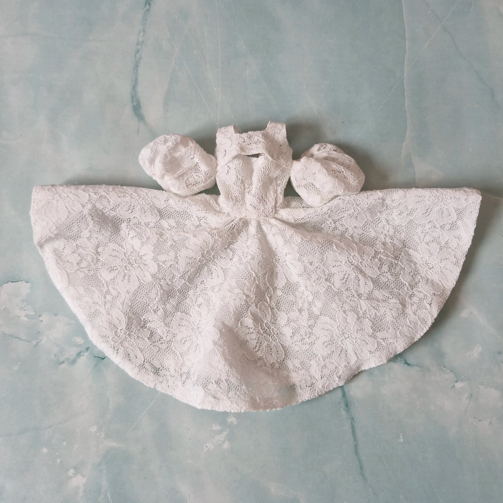 Flat lay of white lace Barbie doll dress with separate puff sleeves on marble background.