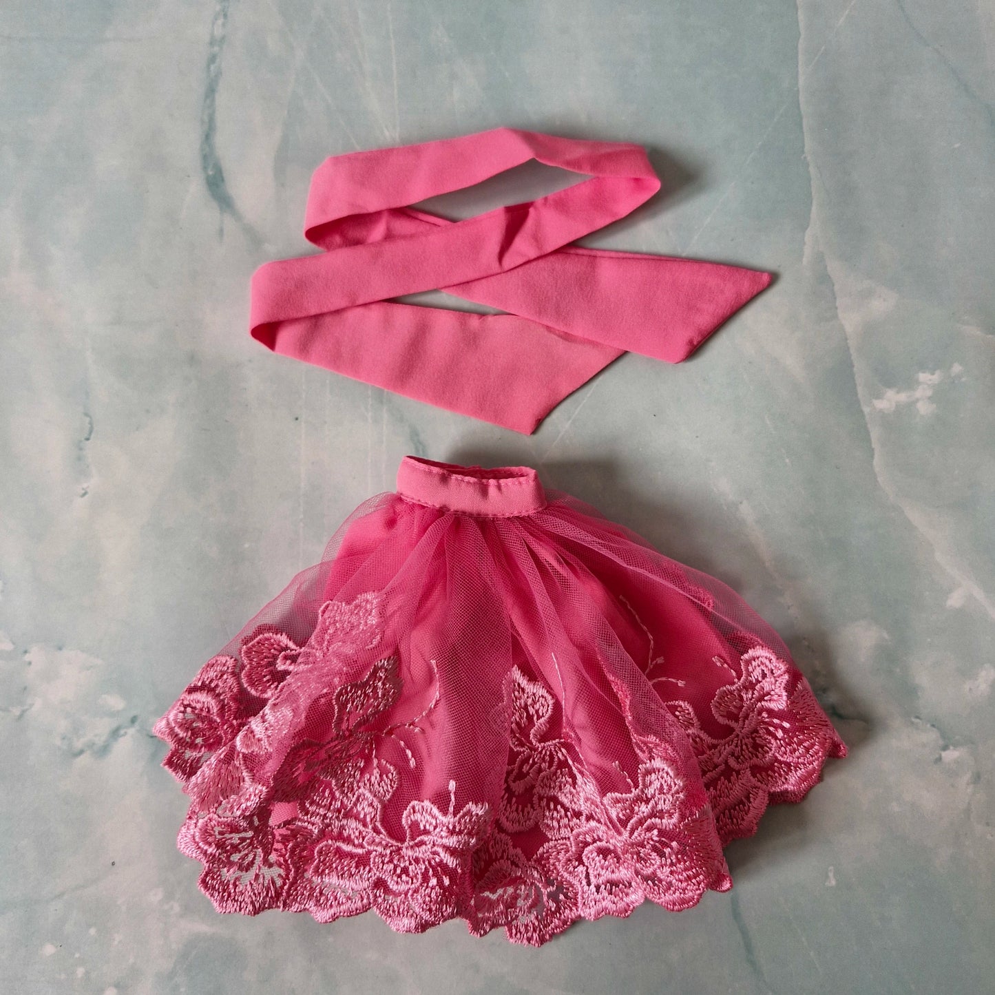 Flat lay of pink lace tulle skirt and pink fabric strip top for Barbie doll.
