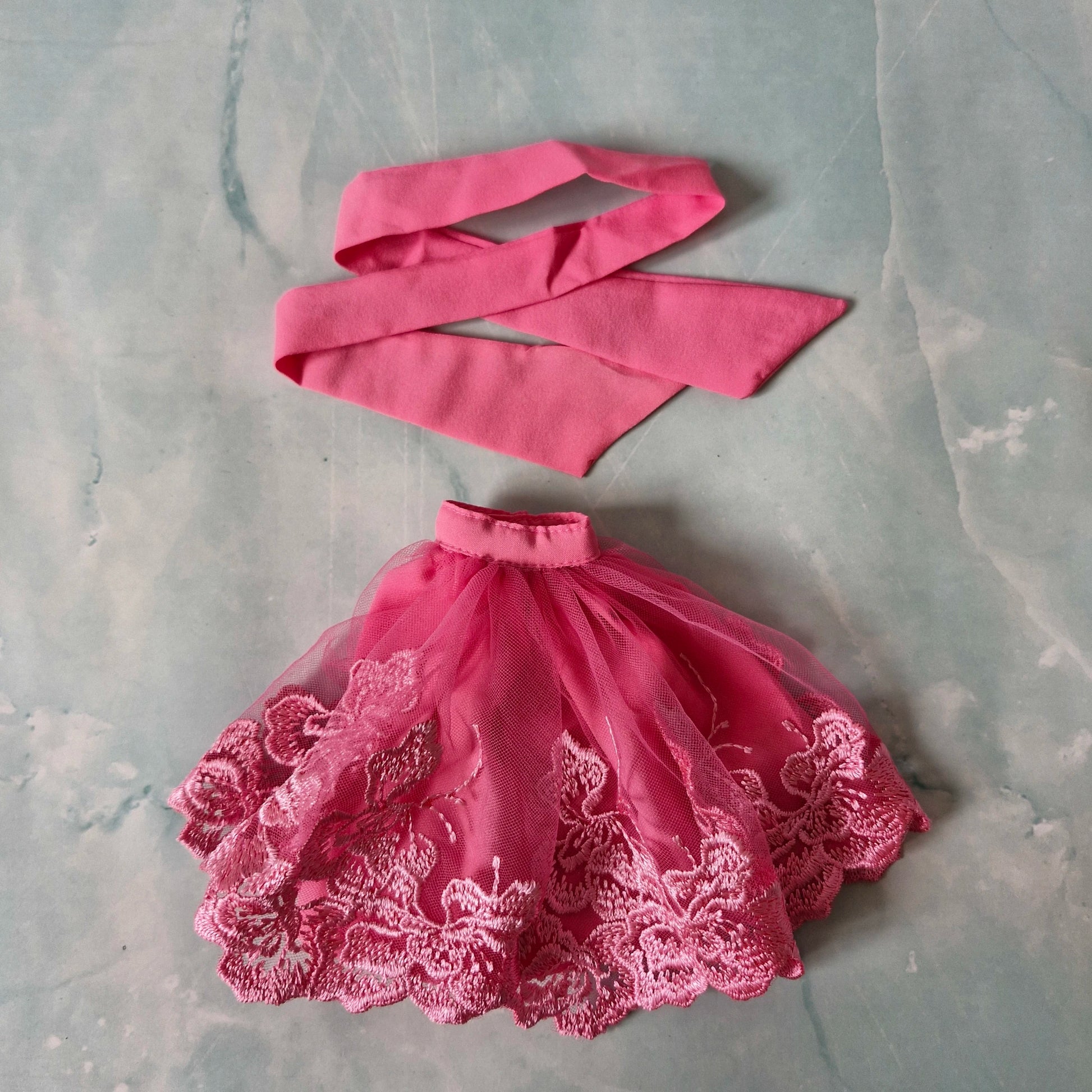 Flat lay of pink lace tulle skirt and pink fabric strip top for Barbie doll.