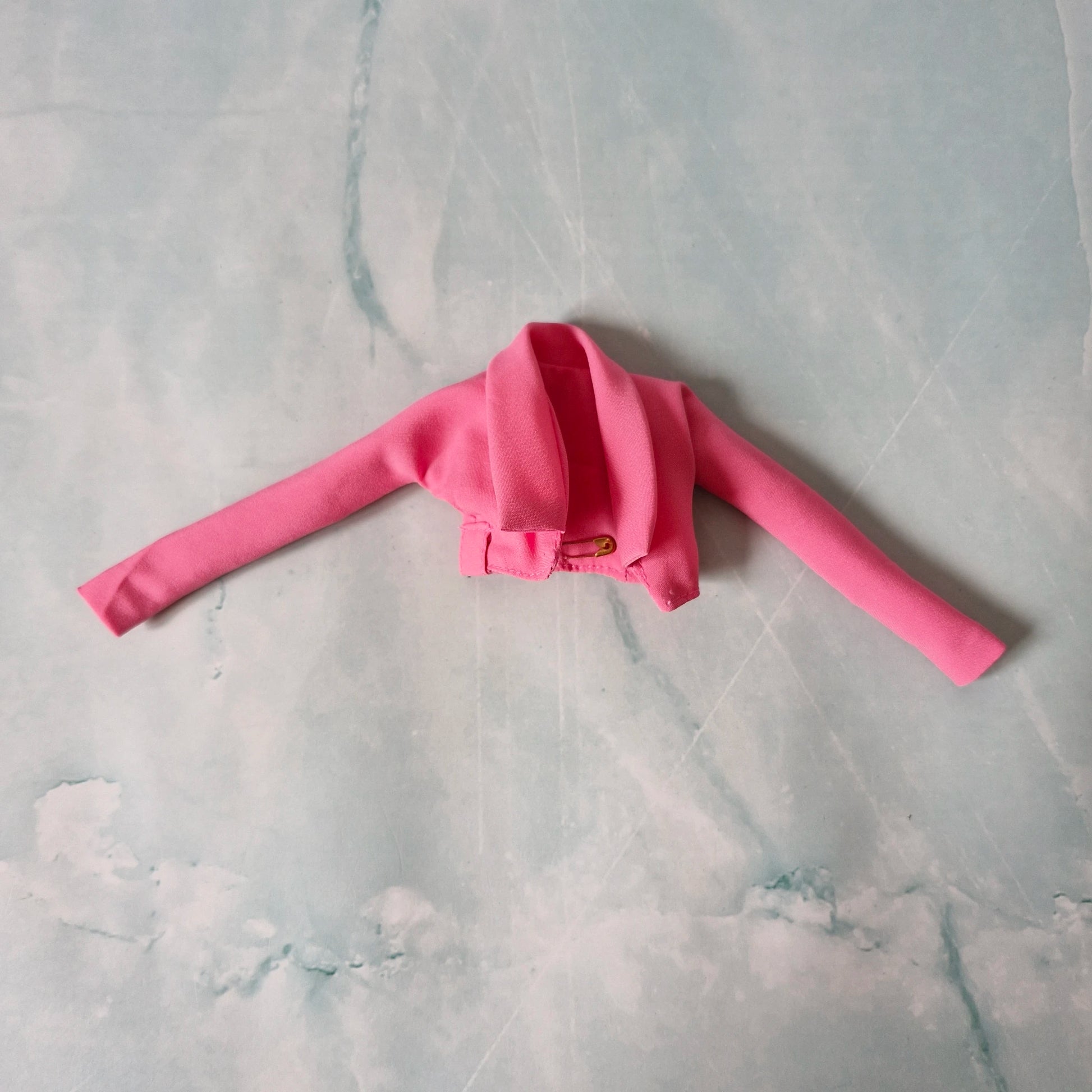 Flat lay of pink cropped jacket for Barbie doll on marble background.