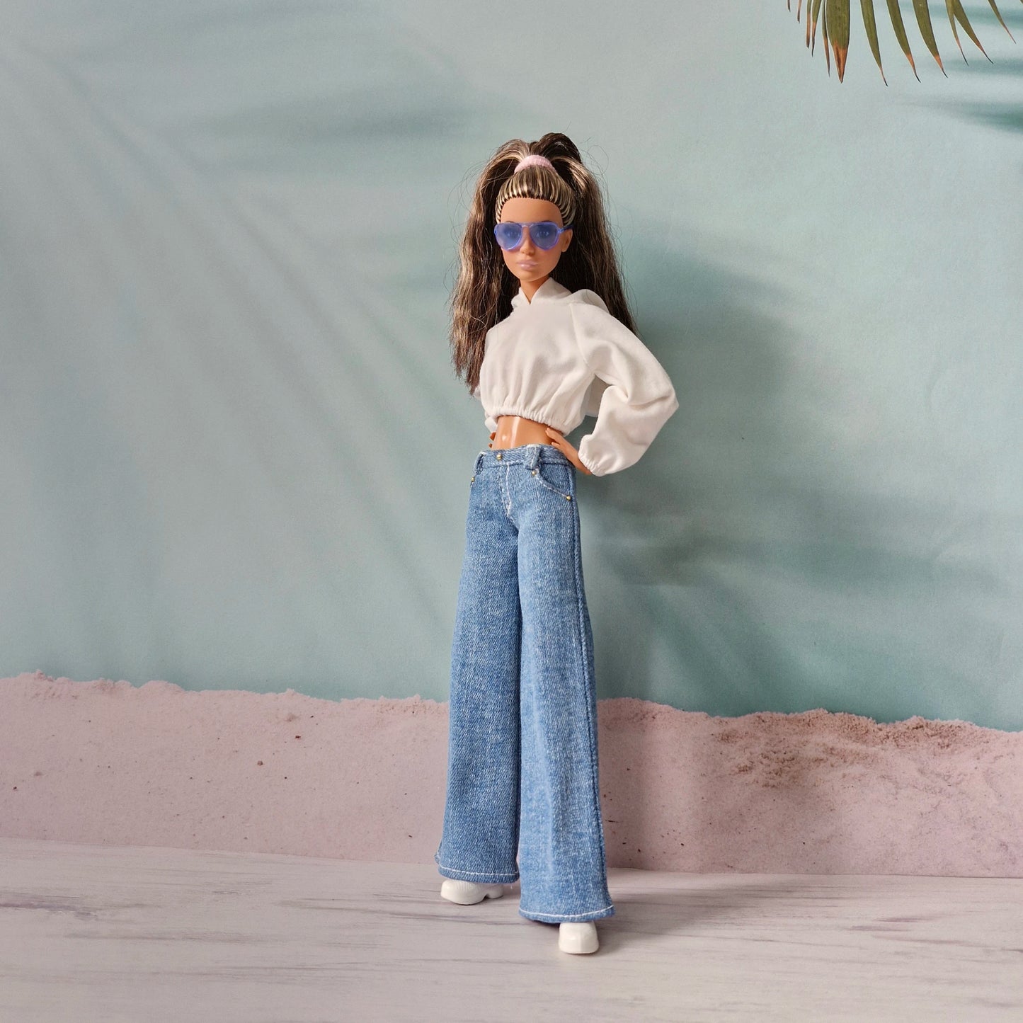 Fashionable Barbie doll wearing white hoodie, dark wash wide-leg jeans, and blue sunglasses.