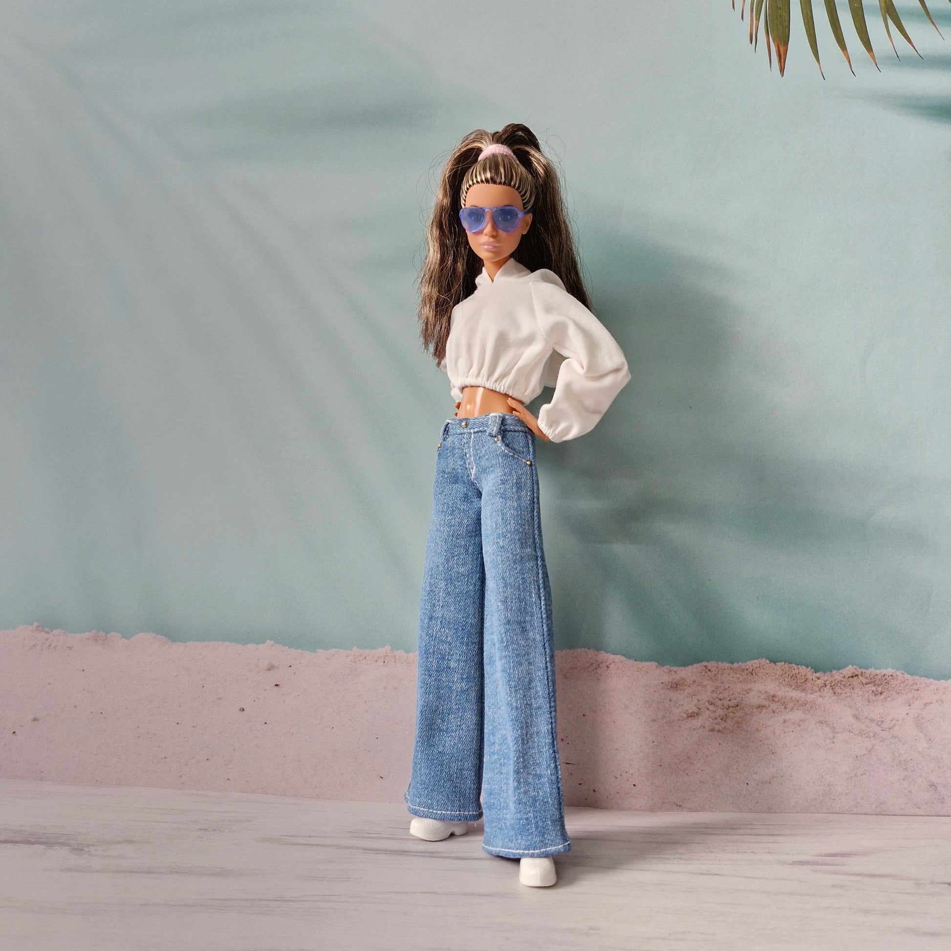 Fashionable Barbie doll wearing white hoodie, dark wash wide-leg jeans, and blue sunglasses.