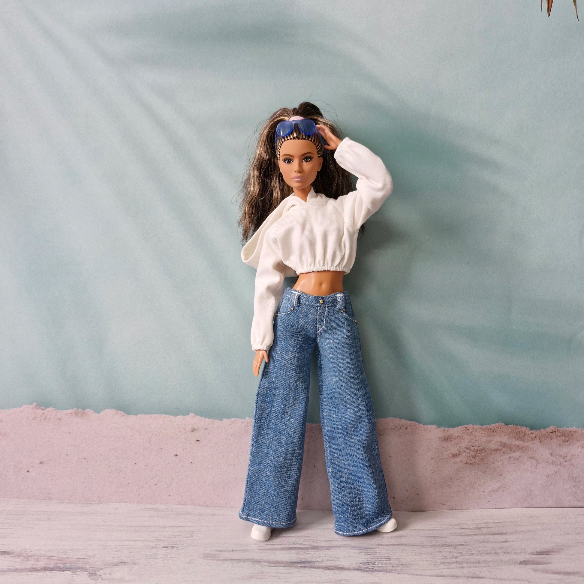 Barbie doll posing in white cropped hoodie and dark wash wide-leg denim jeans.