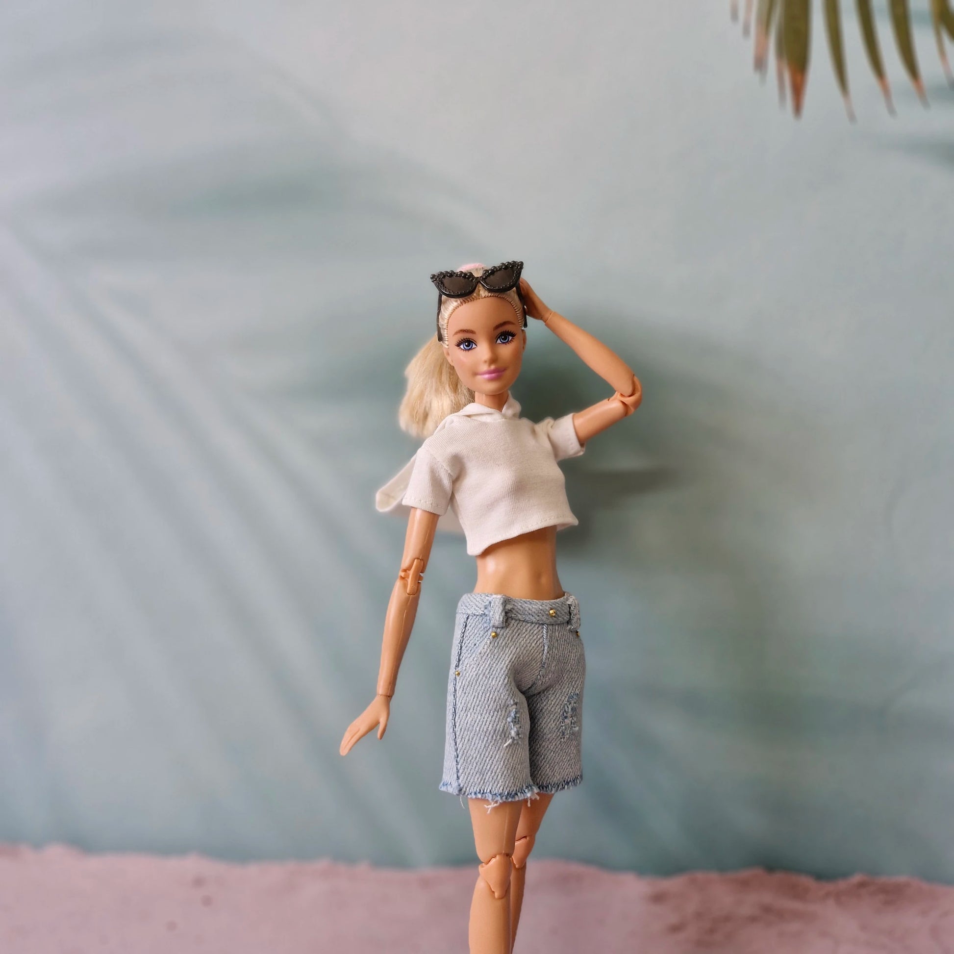 Chic Barbie doll modeling white crop top, denim shorts, and sunglasses on head.