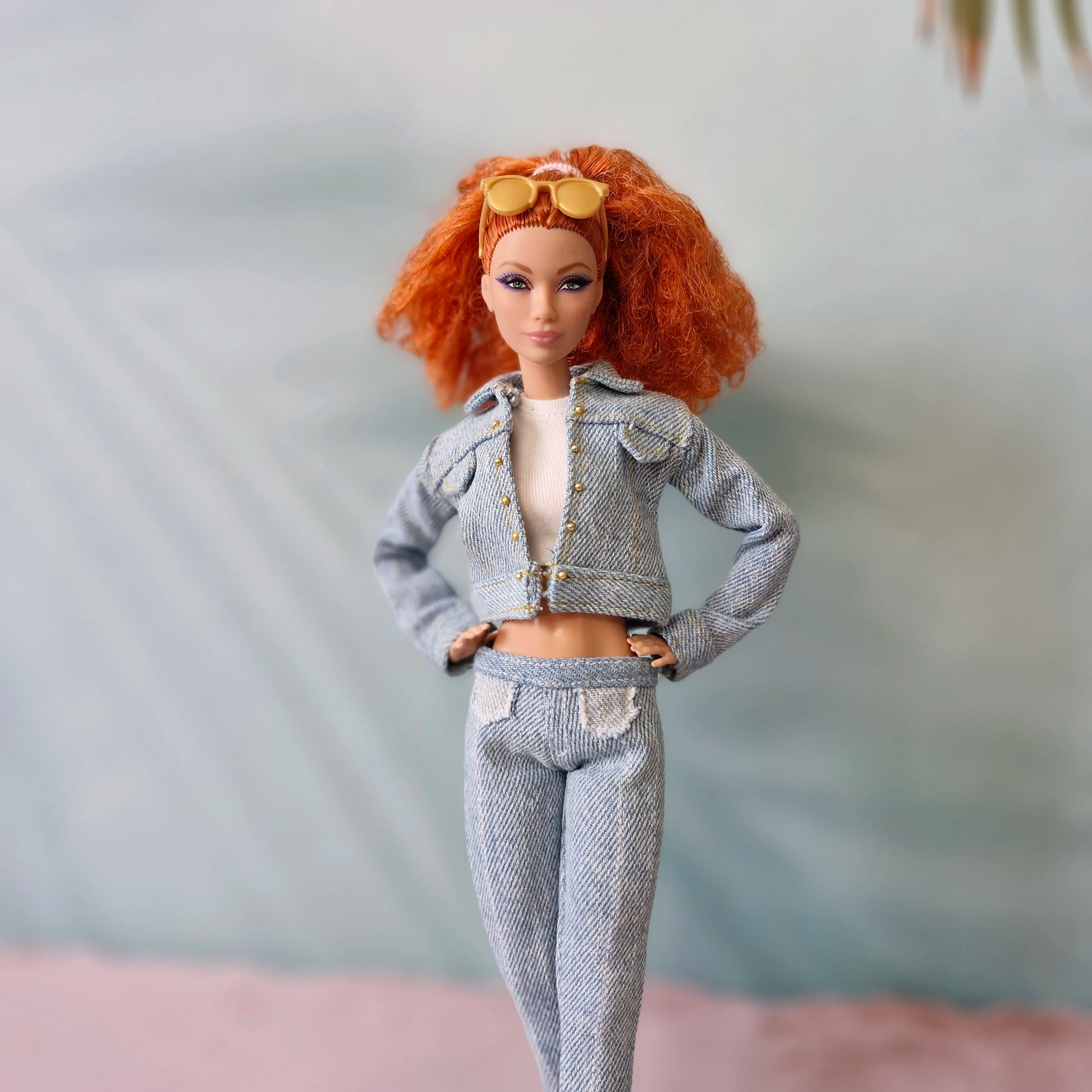 Barbie doll with red hair in full light wash denim outfit with white crop top and sunglasses.