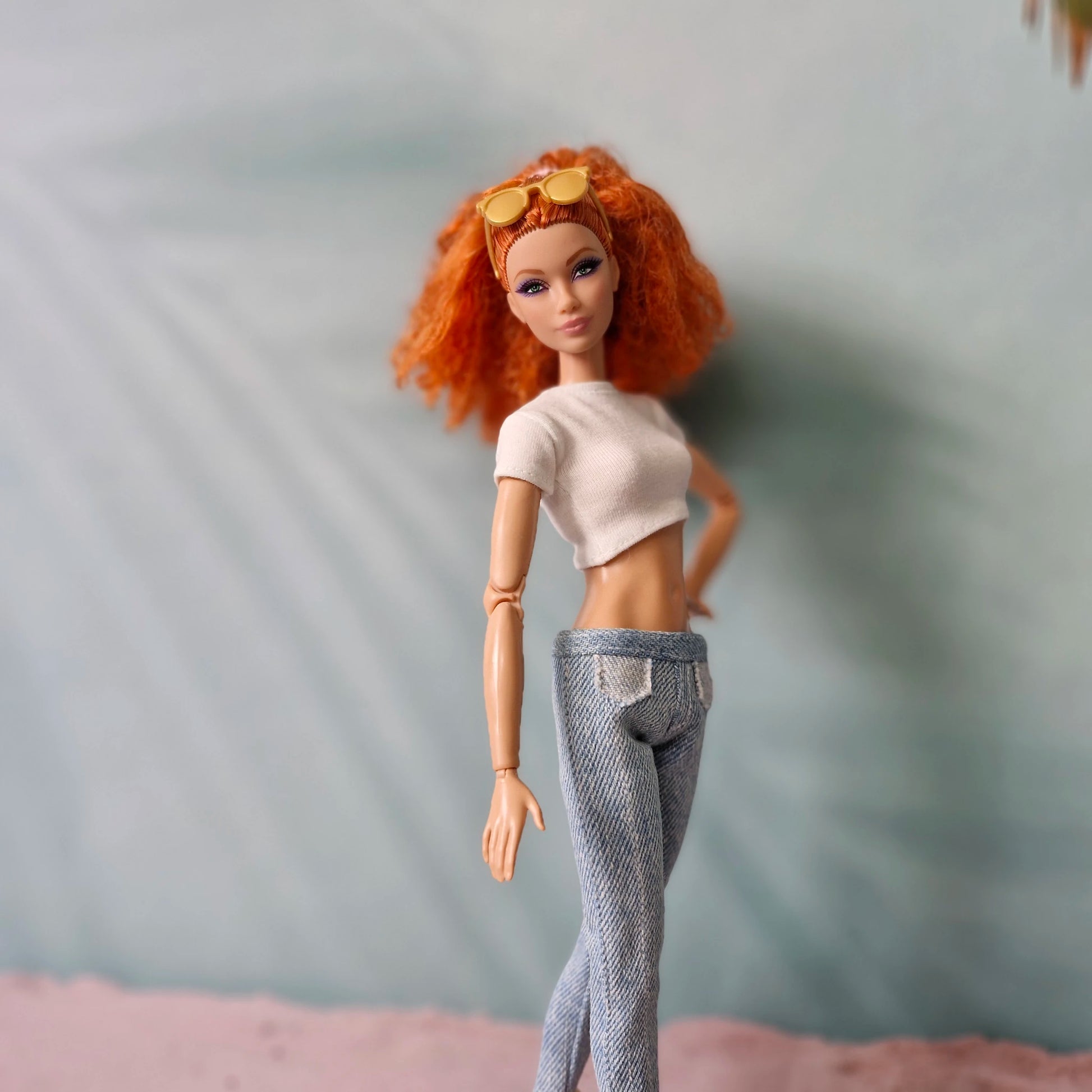 Stylish Barbie doll in white crop top and light wash denim jeans with orange sunglasses.
