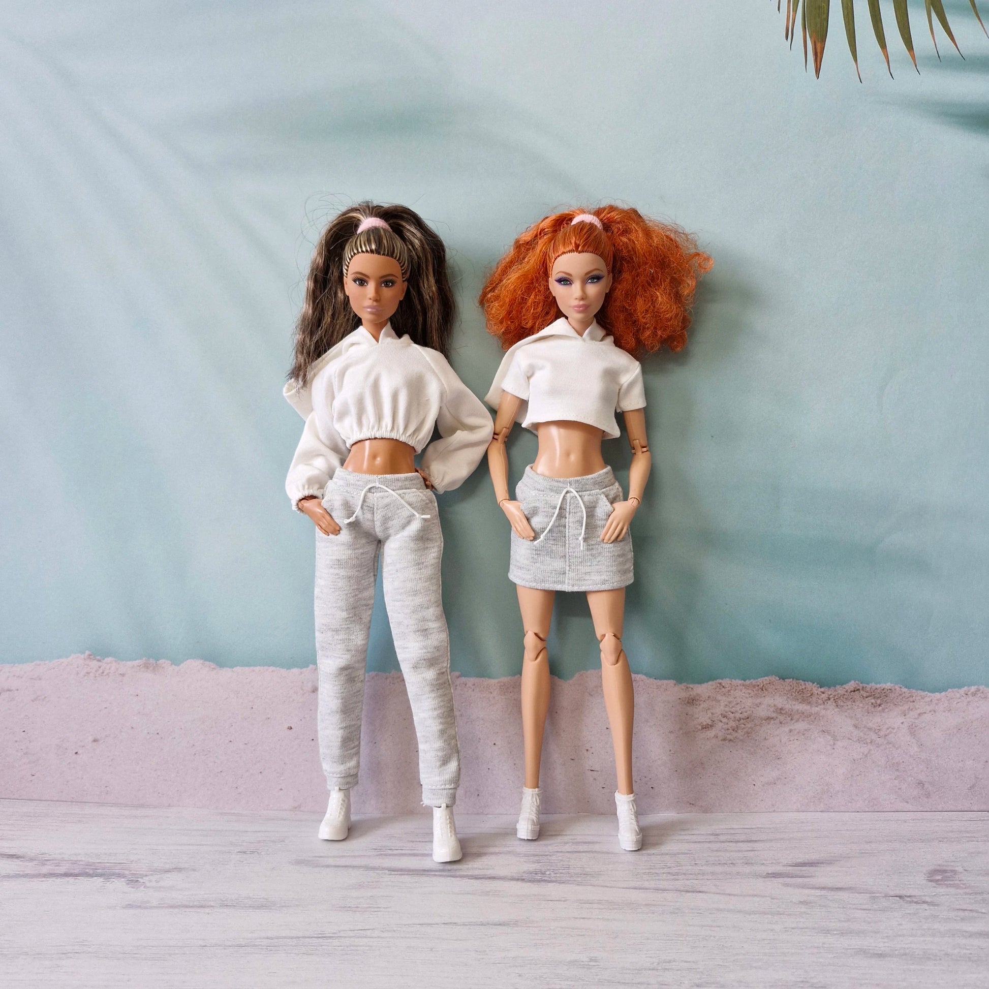 Barbie dolls showcasing white crop tops with grey sweatpants and skirt athleisure sets.