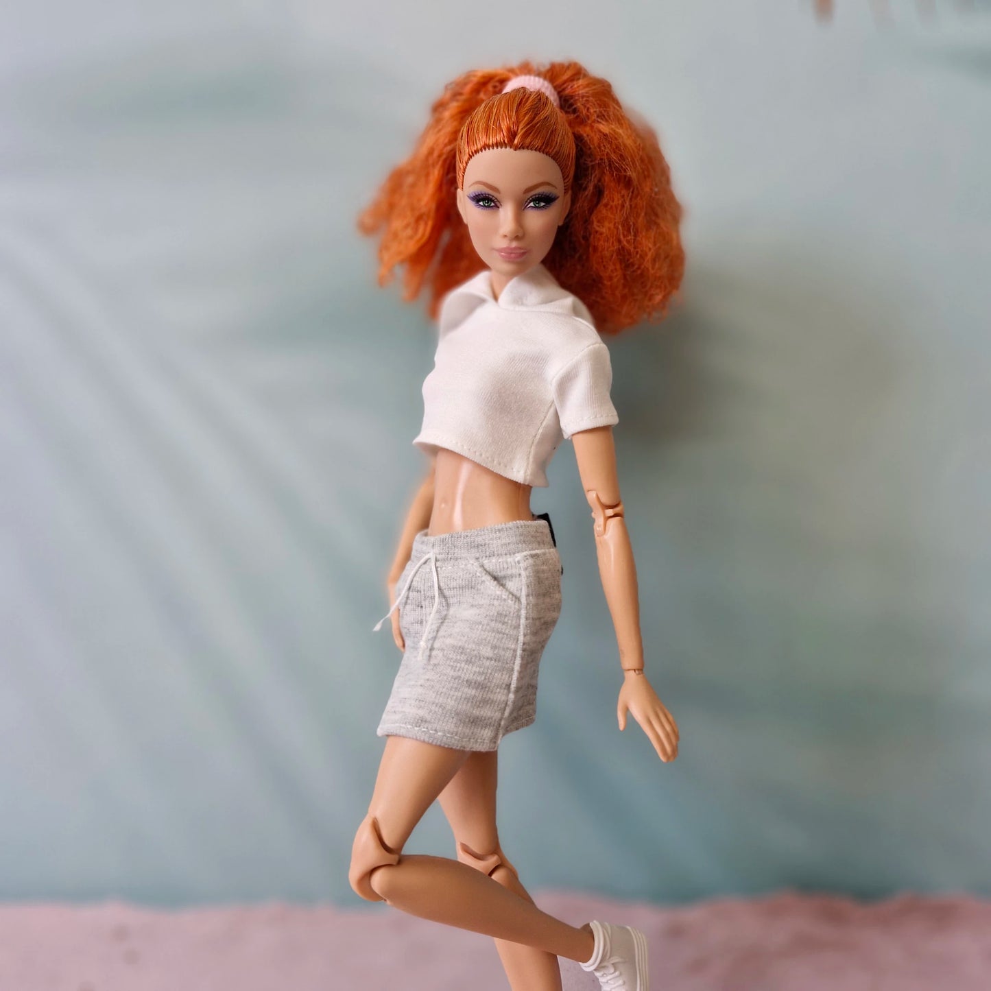 Barbie doll with red hair in white polo crop top and grey sweat shorts athleisure outfit.