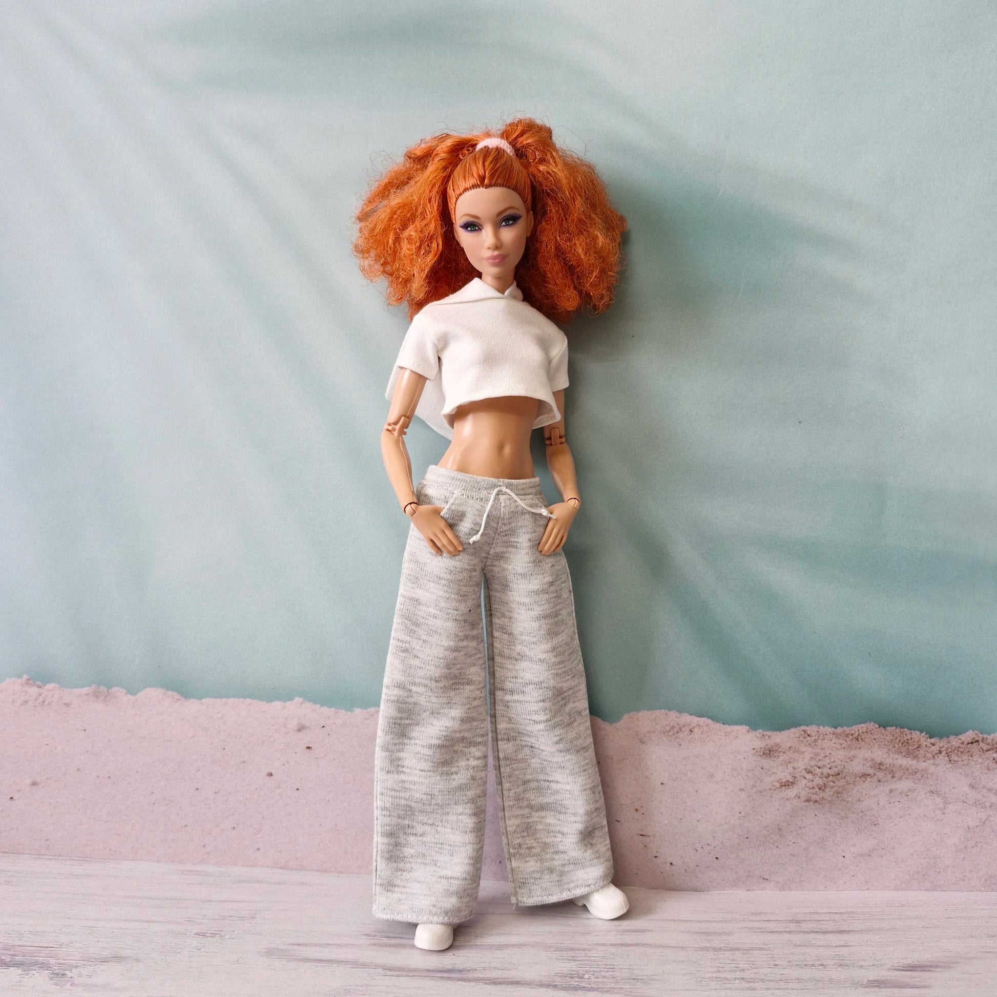 Red-haired Barbie doll models white polo crop top and grey wide-leg sweatpants athleisure style.