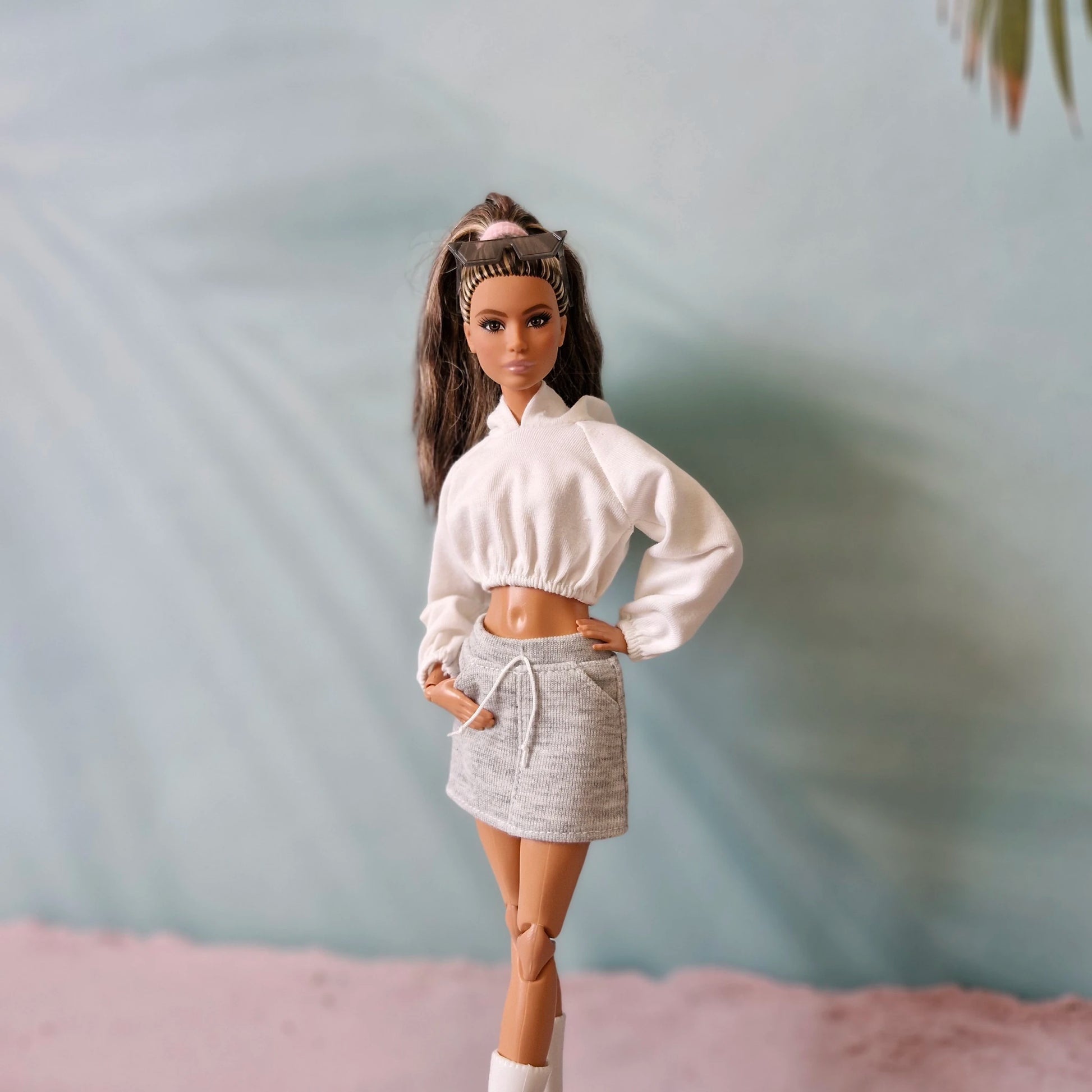 Fashionable Barbie doll wearing white hoodie, grey mini skirt, and sunglasses - athleisure chic.