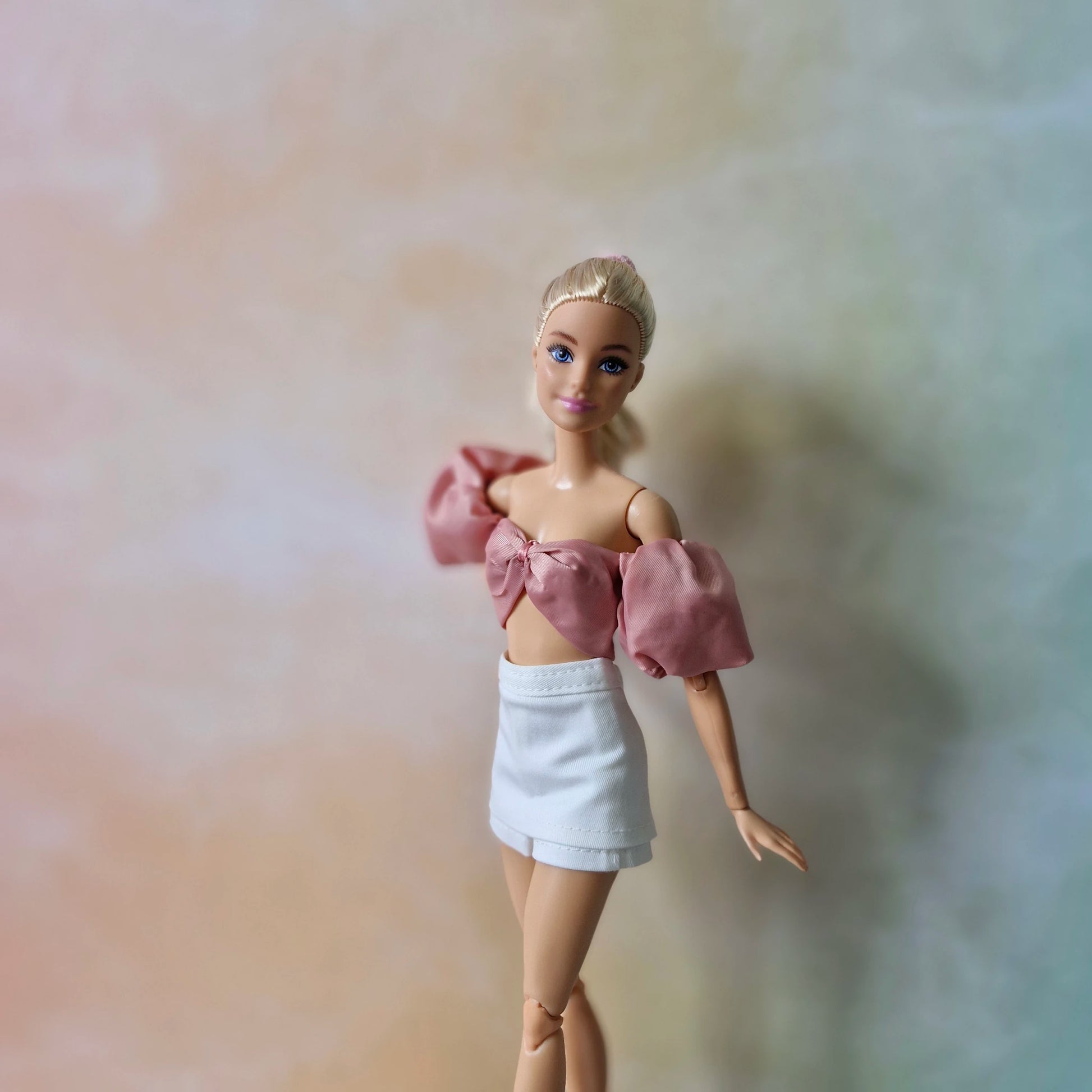 Blonde Barbie doll models dusty rose off-shoulder puff sleeve top with bow and white mini skirt.