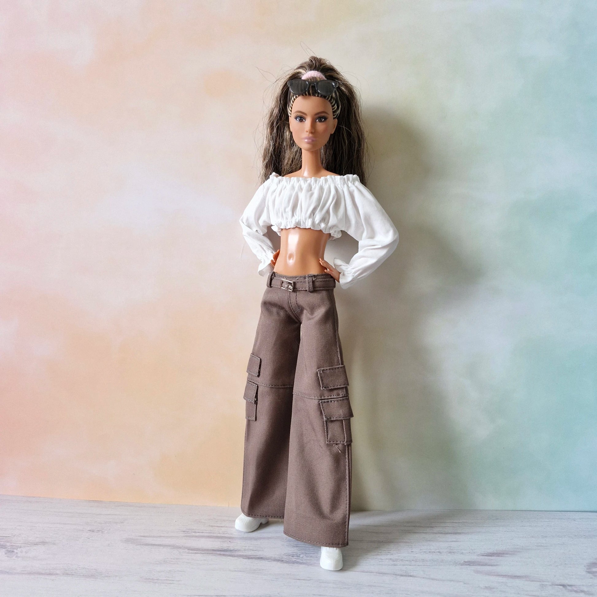 Front view of Barbie doll in white off-shoulder top and brown wide-leg cargo pants, confident stance.