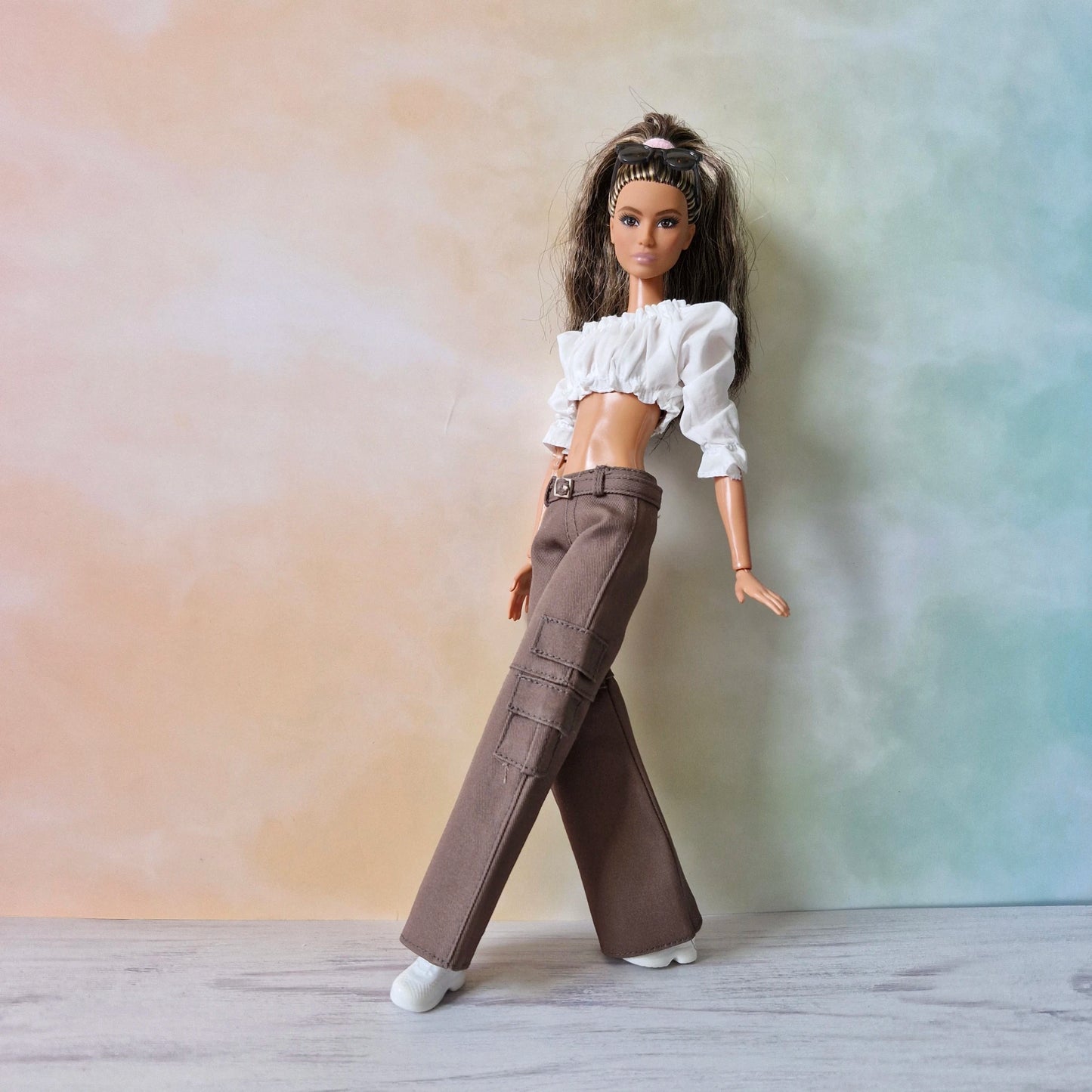 Barbie doll in dynamic pose wearing white crop top and brown wide-leg cargo pants.
