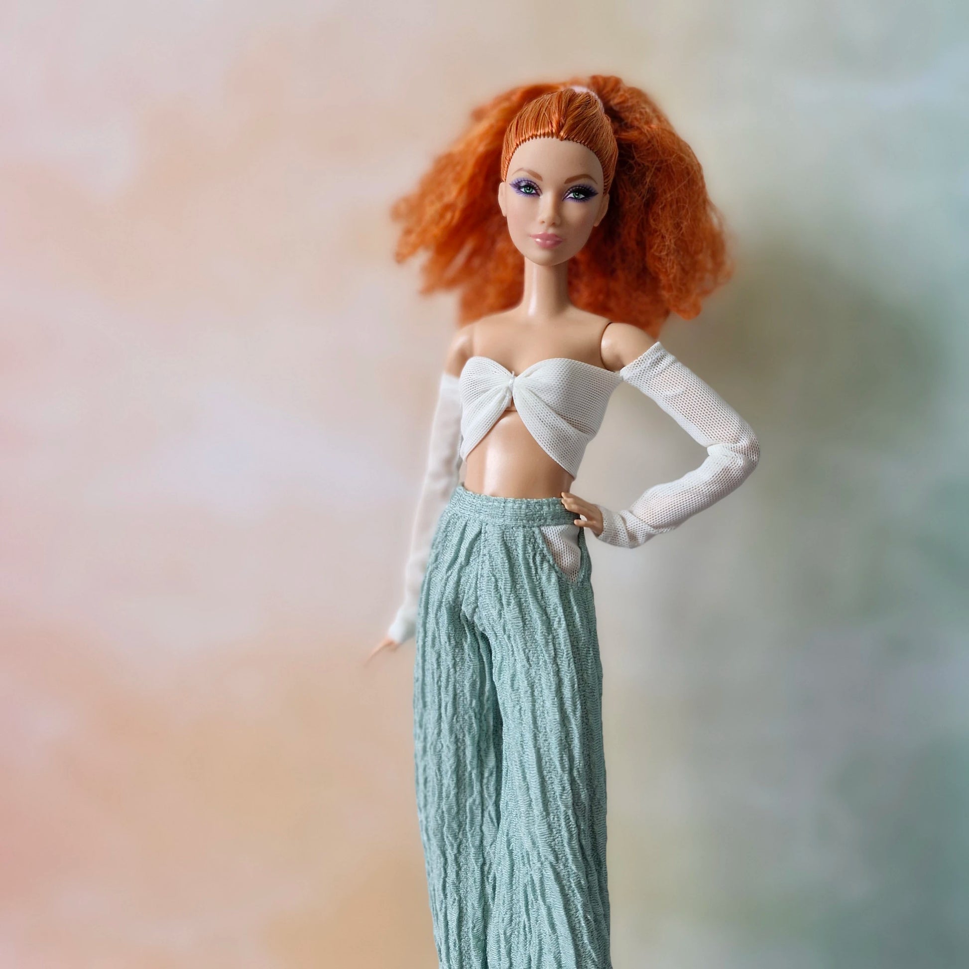 Red-haired Barbie doll in white mesh sleeve twist crop top and mint green textured wide-leg pants, hand on hip.