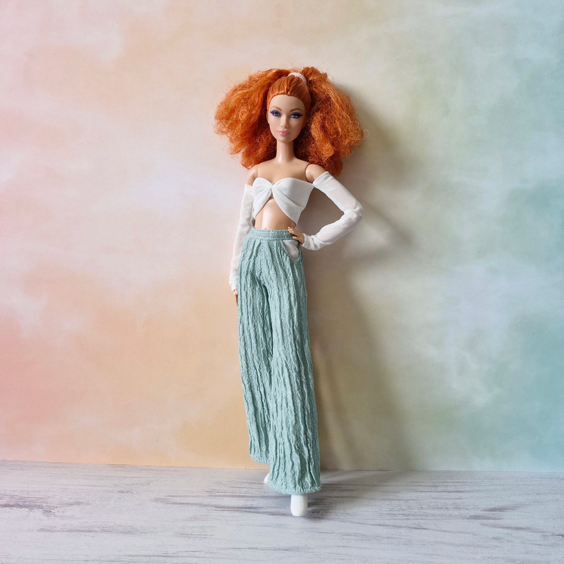 Barbie doll with curly red hair models white off-shoulder twist top and mint green textured palazzo pants.