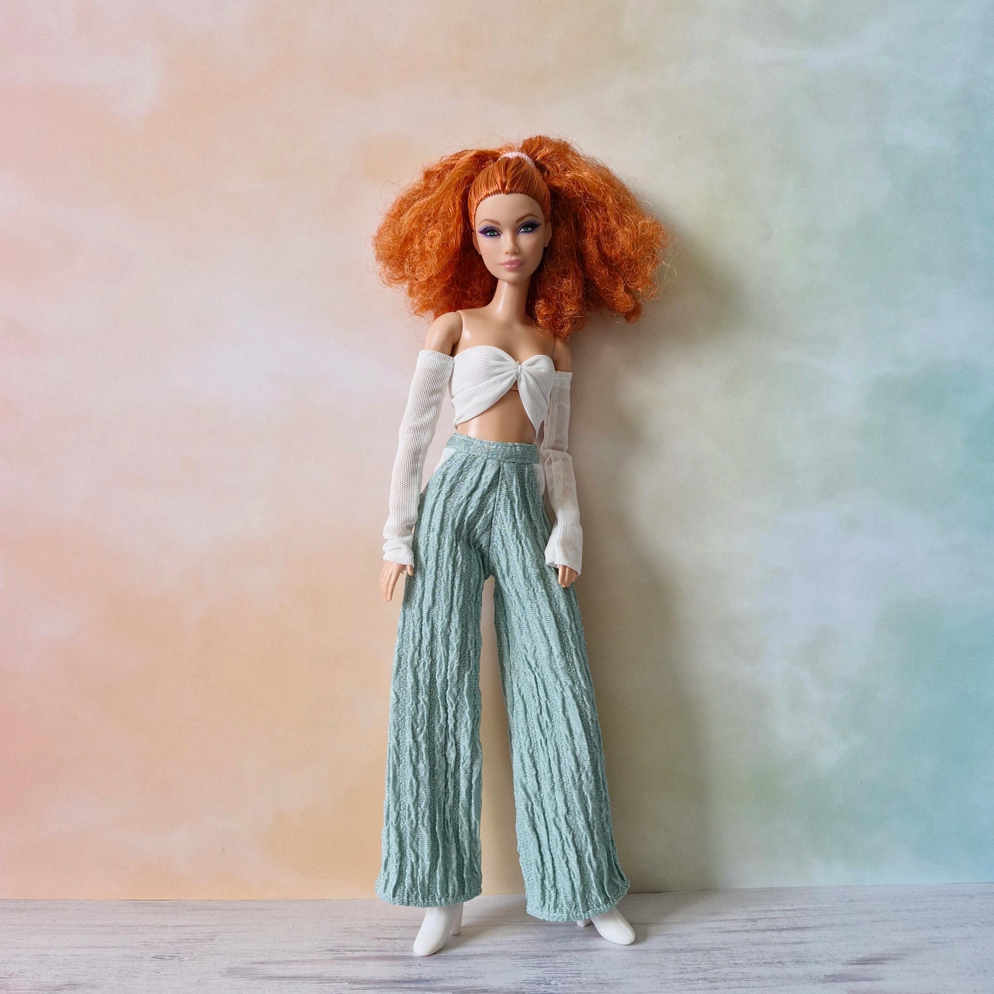 Barbie doll with voluminous red hair wearing white twist front top with mesh sleeves and mint green wide-leg pants.