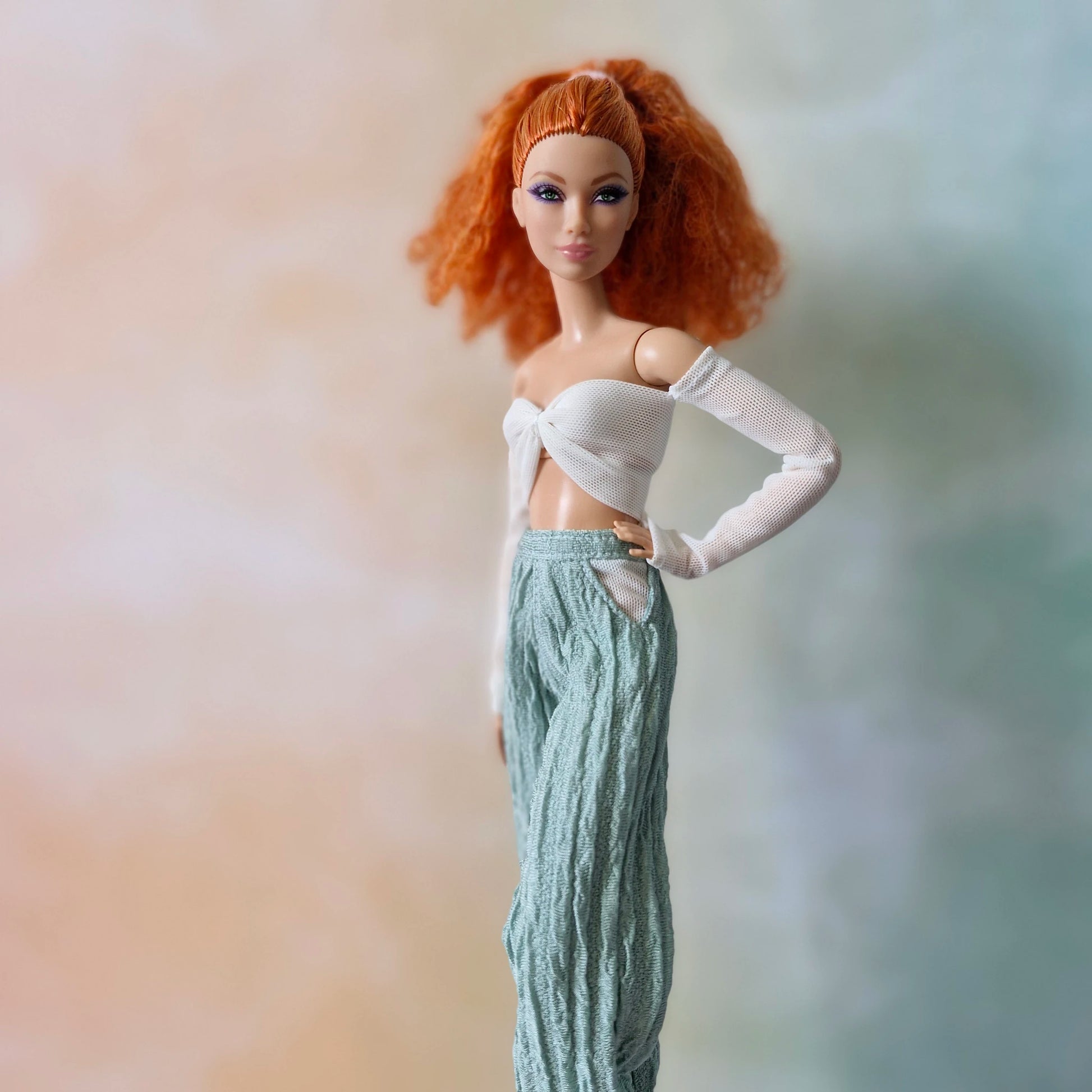 Close-up of red-haired Barbie doll in white off-shoulder mesh sleeve top and mint green textured pants.