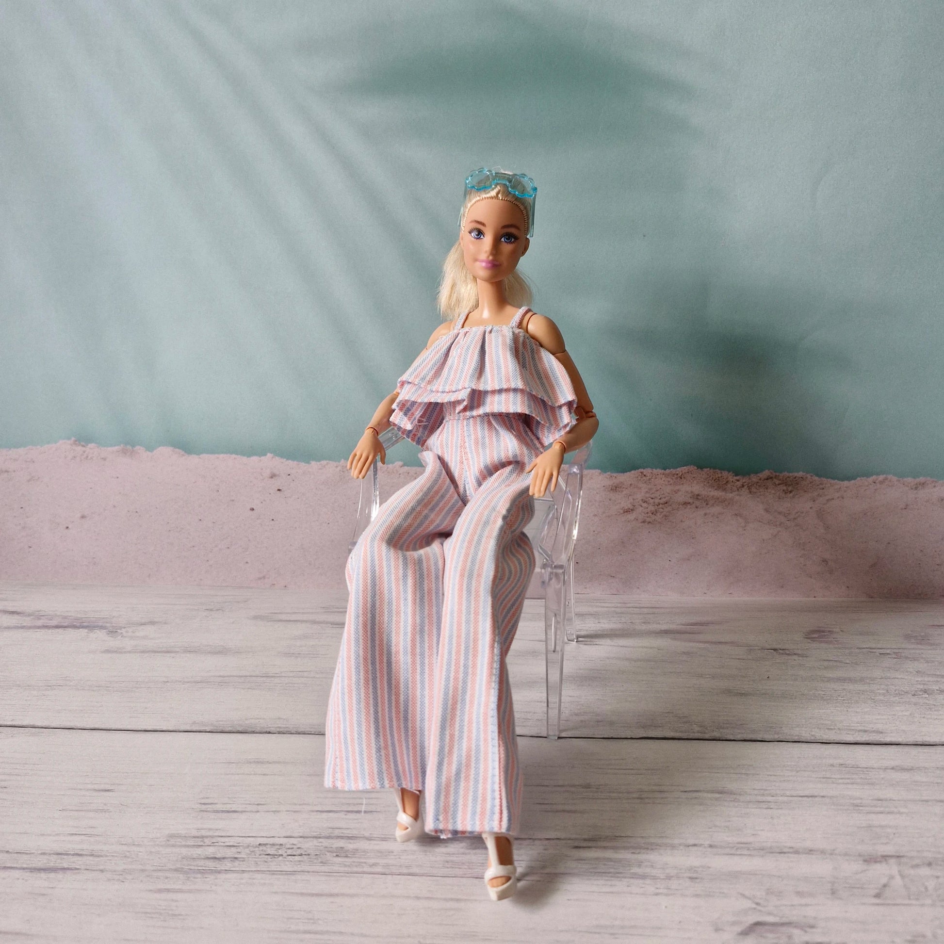 Barbie doll sitting on a clear miniature chair wearing striped ruffle jumpsuit.