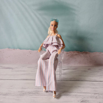 Barbie doll sitting on a clear miniature chair wearing striped ruffle jumpsuit.