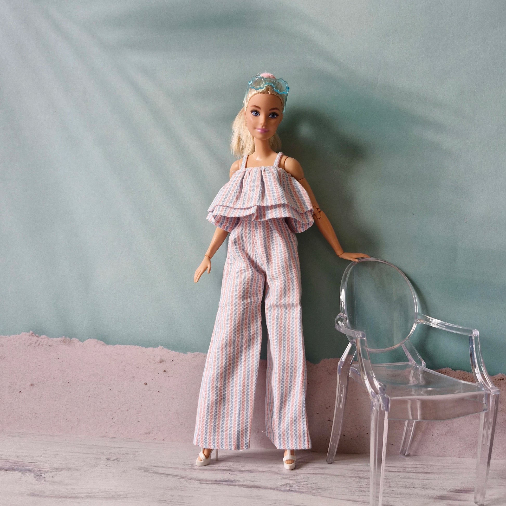 Barbie doll in summer striped jumpsuit with ruffle neckline, next to clear ghost chair.
