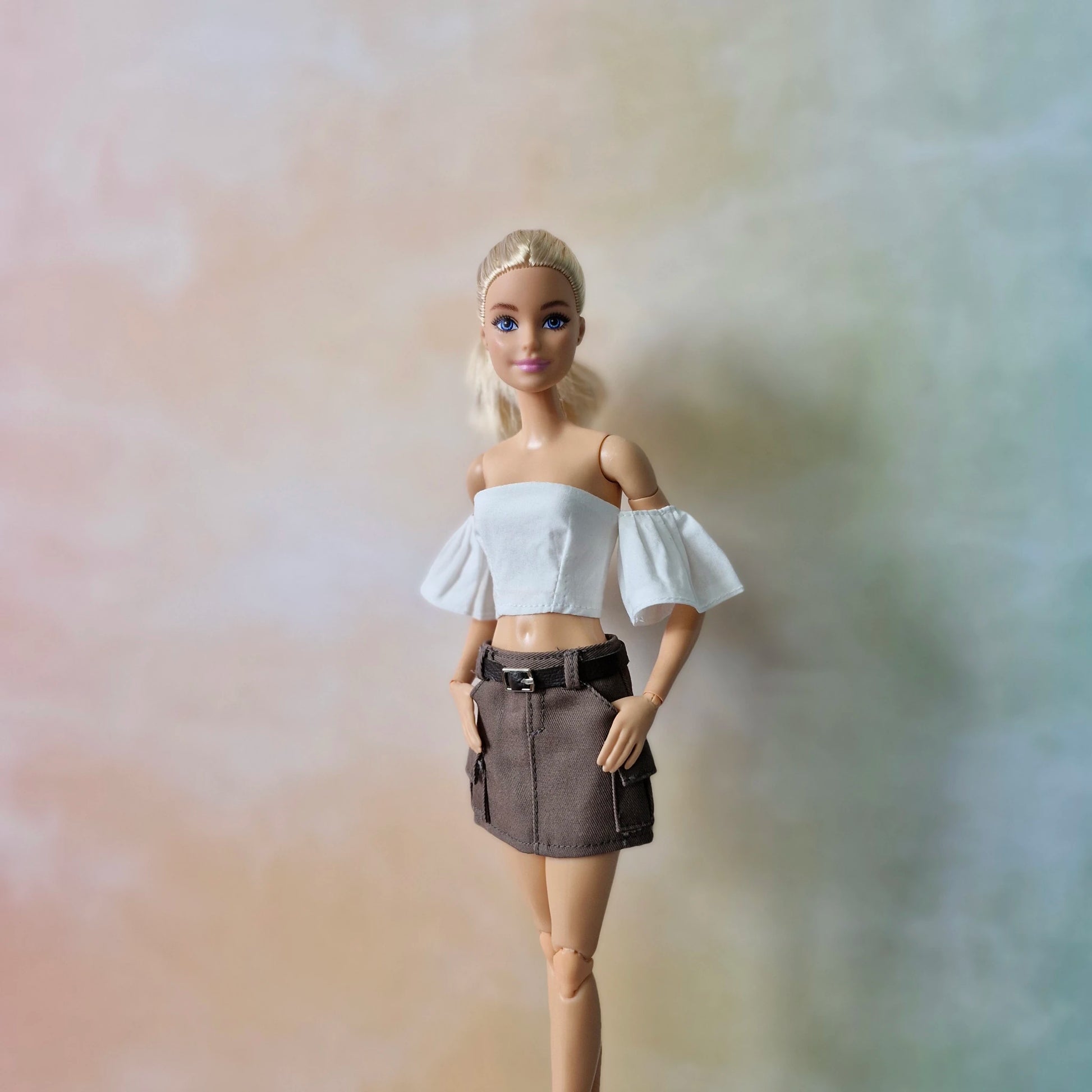 Barbie doll with hands in pockets of brown cargo mini skirt, wearing white crop top.